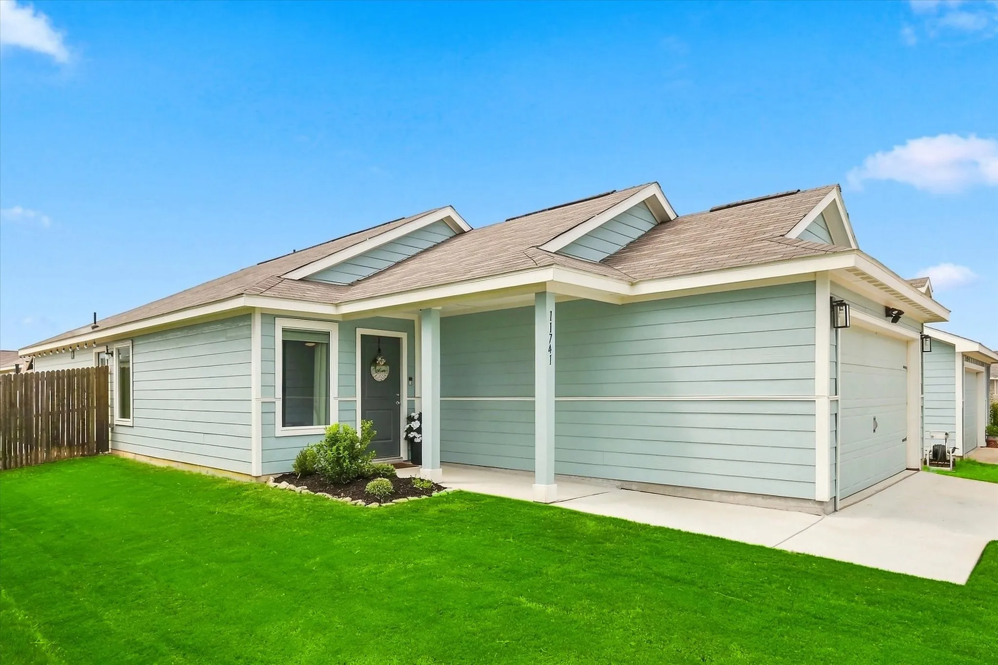 Light blue siding exterior with a covered front porch, attached garage, and a fenced side yard