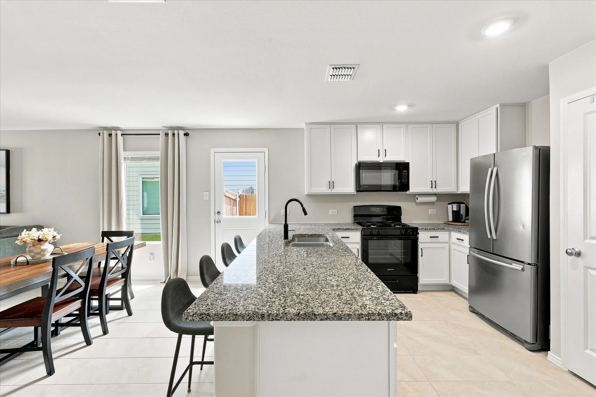 Kitchen featuring a granite-finish island, stainless steel refrigerator, white cabinetry, and recessed lighting