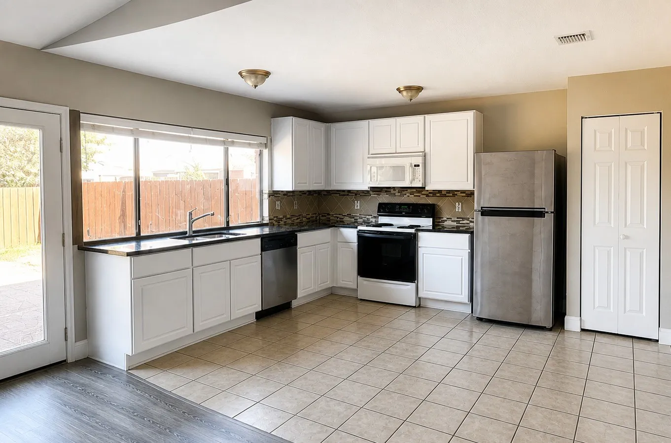 Kitchen featuring white cabinetry, dark countertops, tiled backsplash, stainless steel appliances, and a glass-paneled door