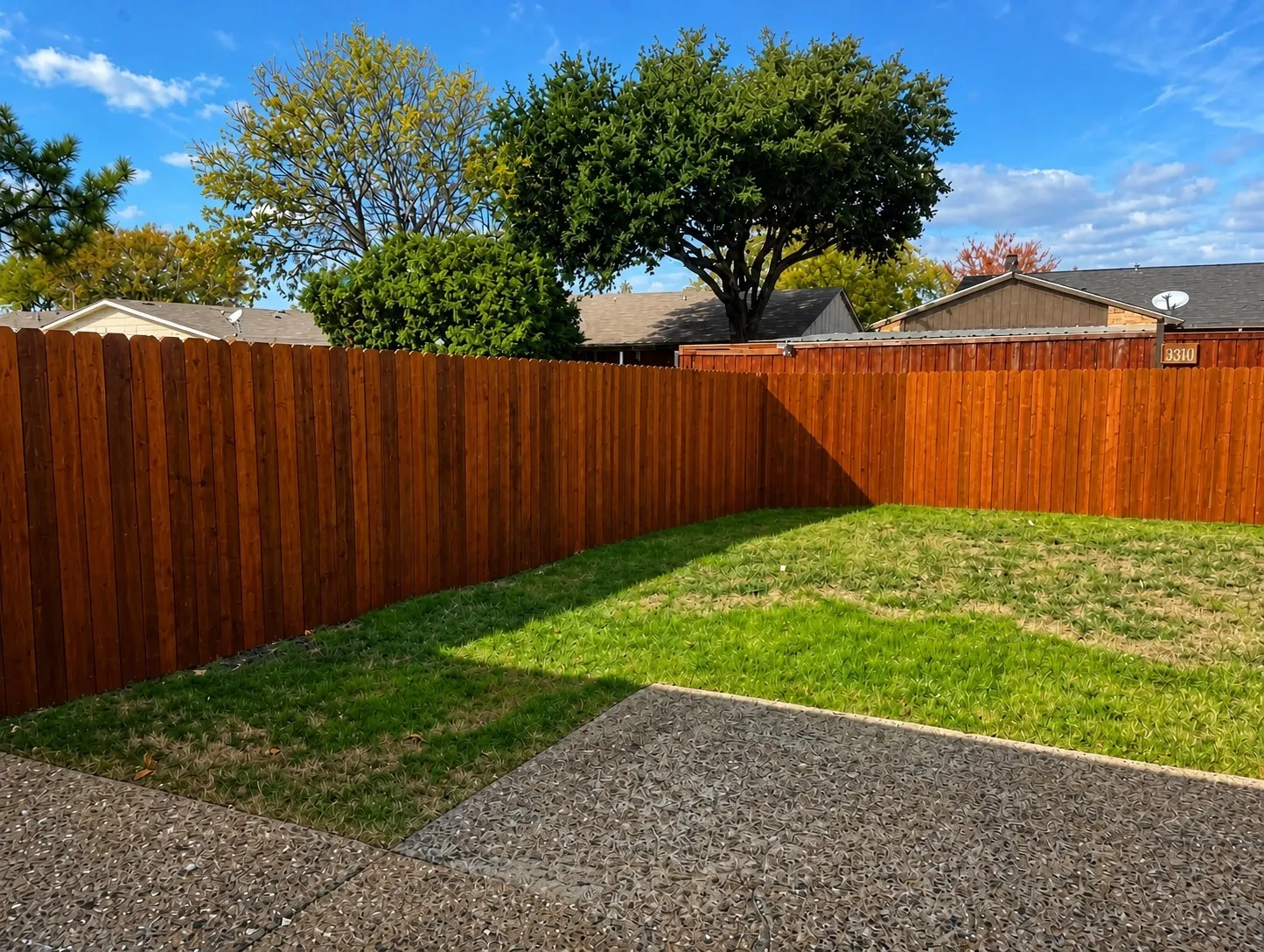 Backyard featuring a stained privacy fence, natural grass area, and exposed aggregate concrete patio