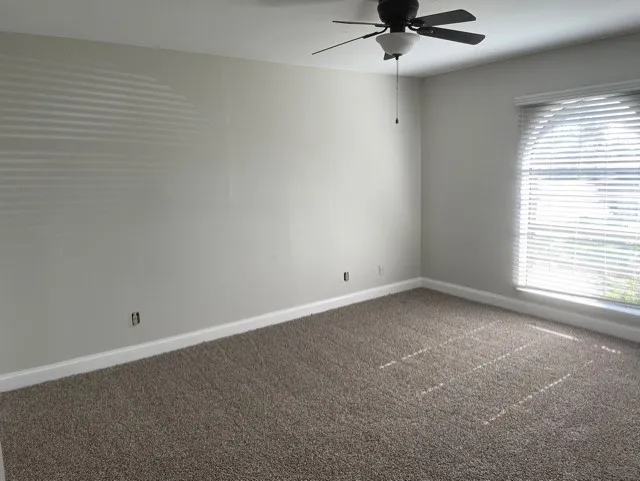 Carpeted flooring, ceiling fan with integrated lighting, window with blinds, and white trim