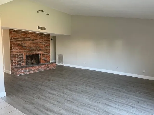 Vaulted ceiling, brick fireplace, wood-finish flooring, and neutral wall tones