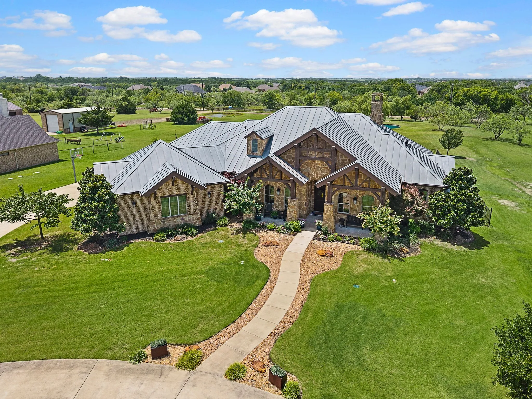 An impressive aerial view highlights the home’s grand design, sweeping walkway, manicured lawn & spacious surroundings.