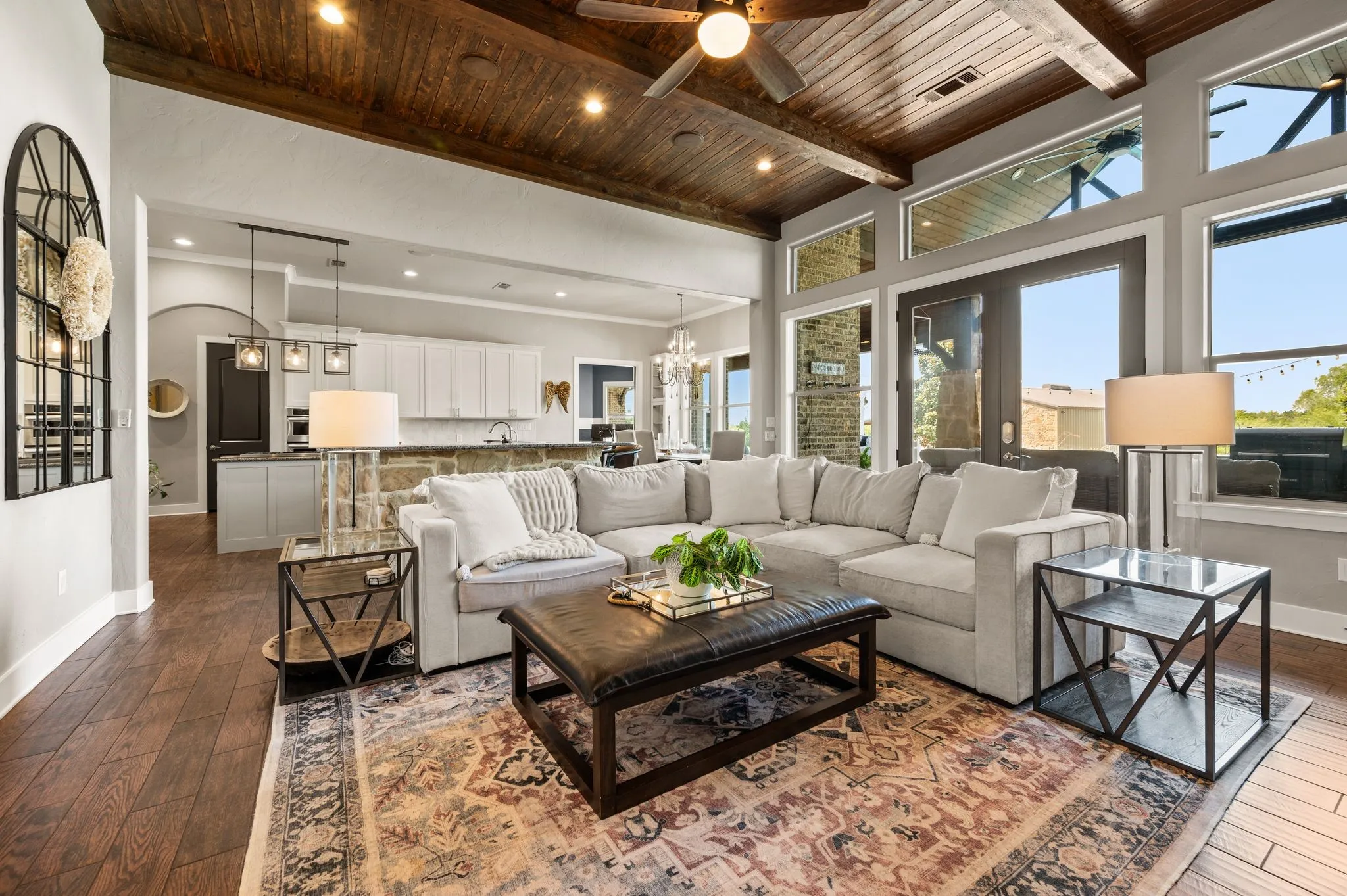 The bright living room delivers serious wow factor with a wood-plank ceiling, exposed beams, walls of windows & seamless flow into the kitchen.
