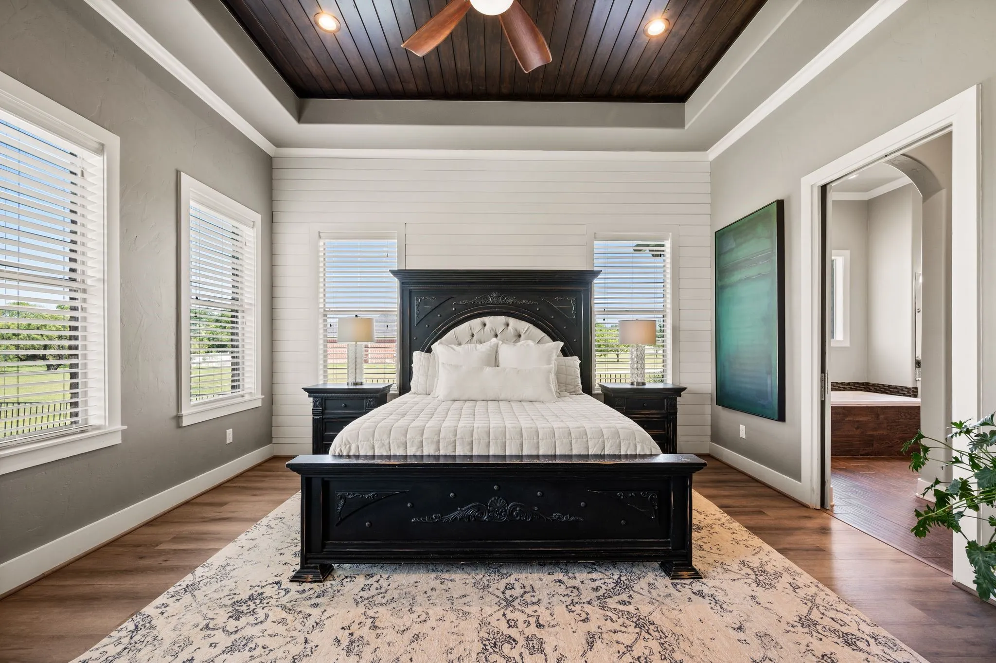 The spacious primary suite feels like a private retreat with a dramatic wood-inset tray ceiling, shiplap accent wall & abundant natural light.