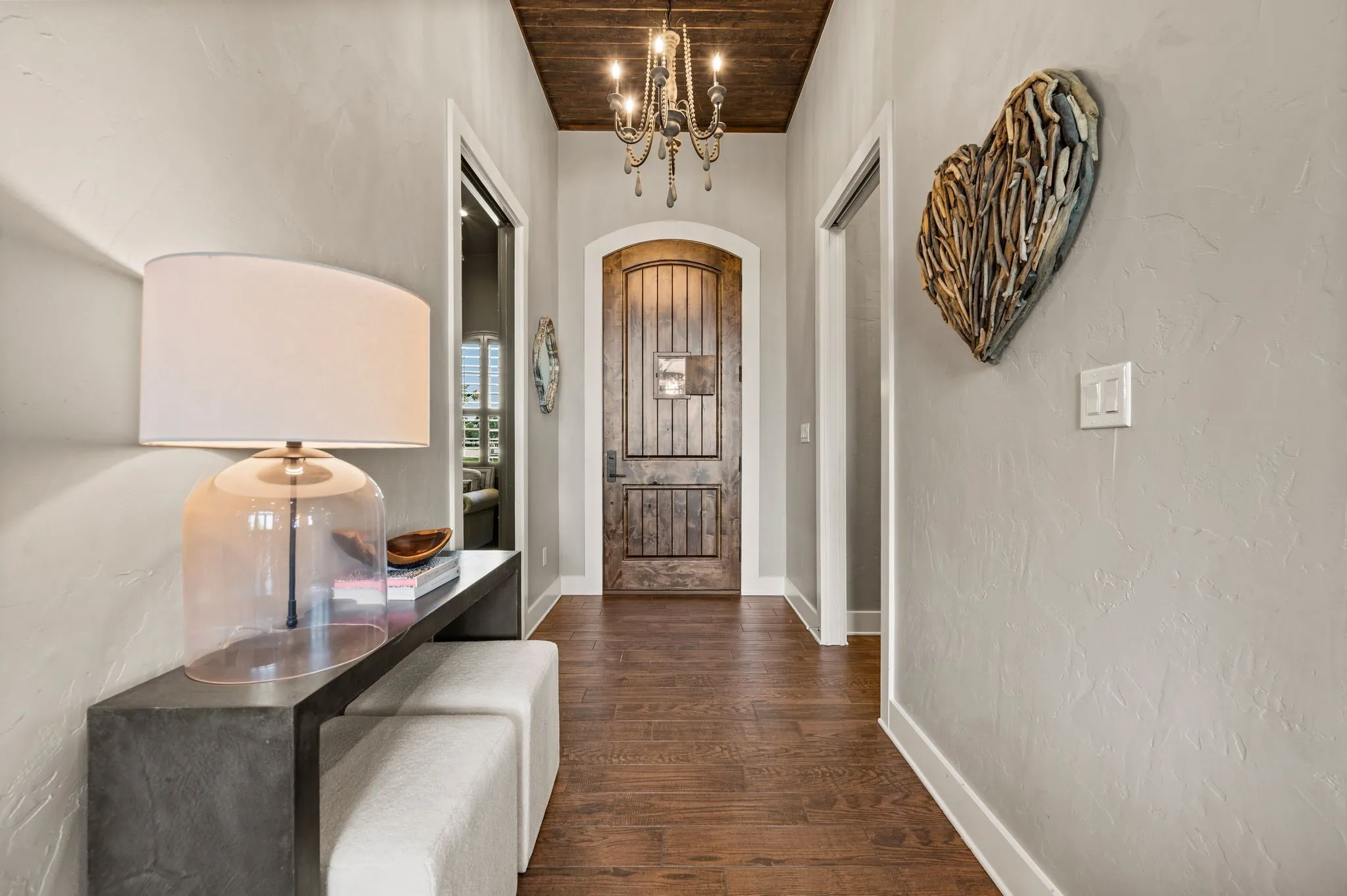 A warm & stylish entry features tile wood-like flooring, a statement chandelier, wood-plank ceiling detail & beautiful arched front door.