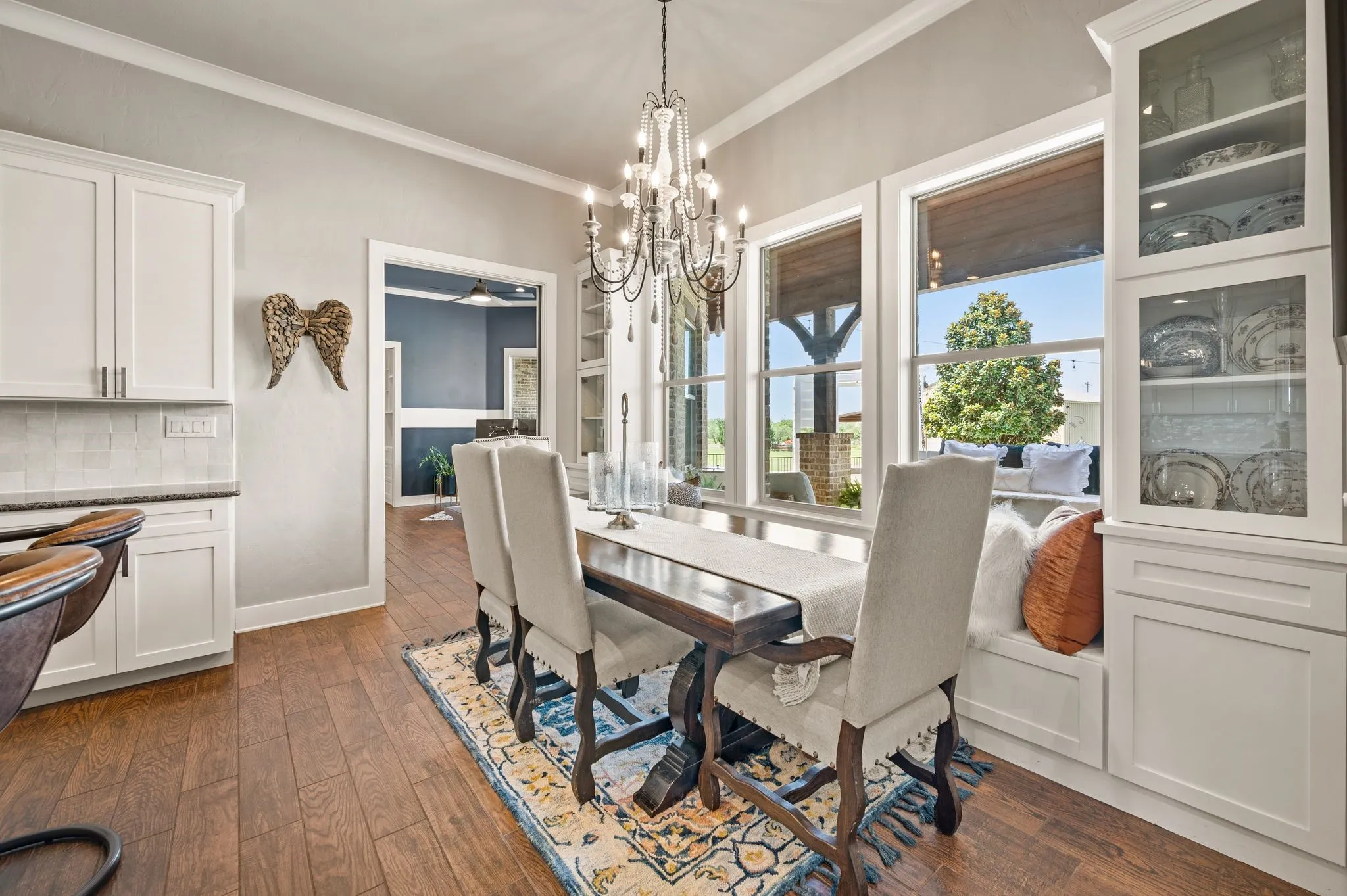 The elegant dining area features a sparkling chandelier, custom display cabinetry & oversized windows overlooking the covered patio.