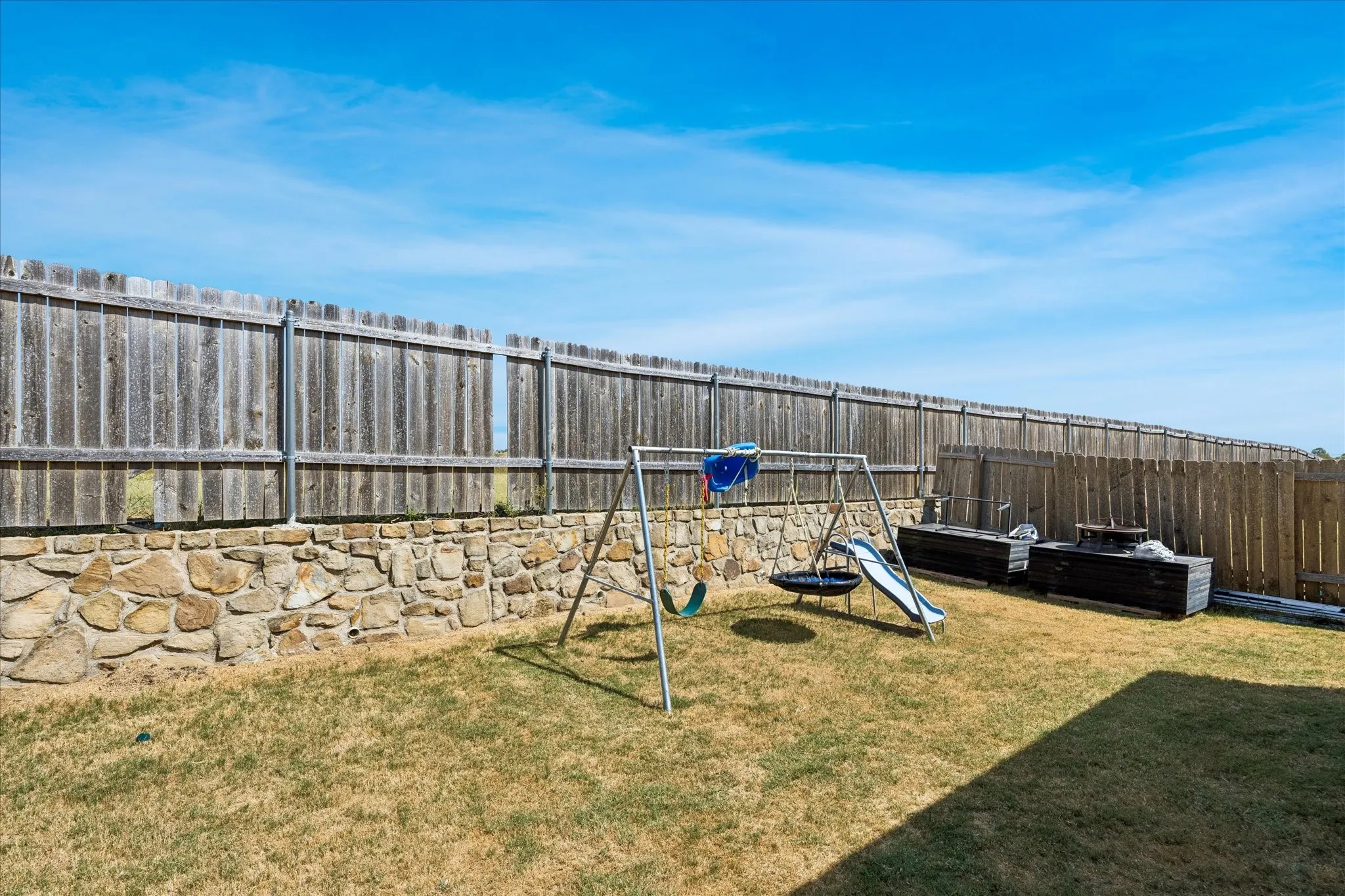 Expansive backyard featuring a natural stone retaining wall, wood privacy fencing, and an open grass area
