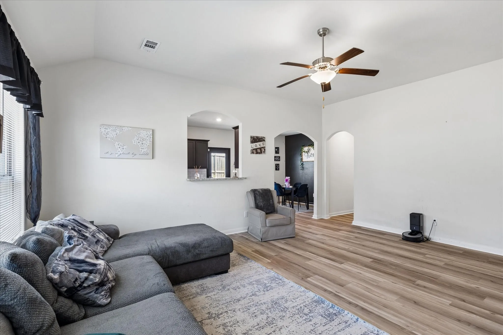 Spacious living area featuring warm wood-finish flooring, recessed lighting, and a ceiling fan with brushed metal finish