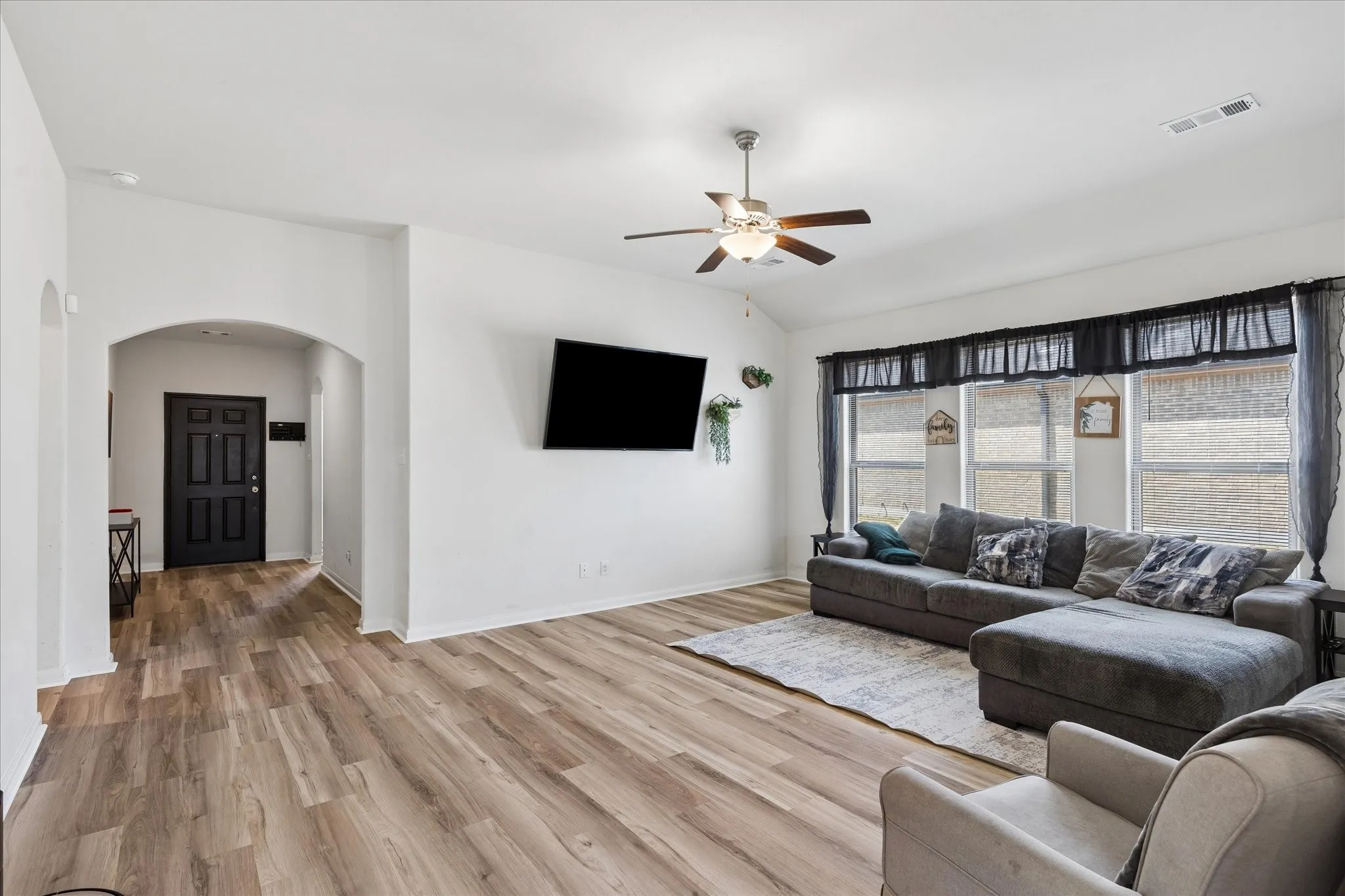 Vaulted ceiling, wood-finish flooring, ceiling fan with integrated lighting, multiple windows, and a dark paneled entry door
