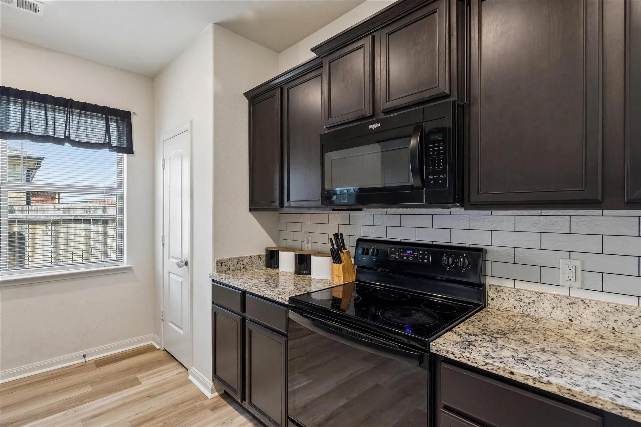 Kitchen featuring dark wood cabinetry, light-colored speckled countertops, white subway tile backsplash, and wood-finish flooring