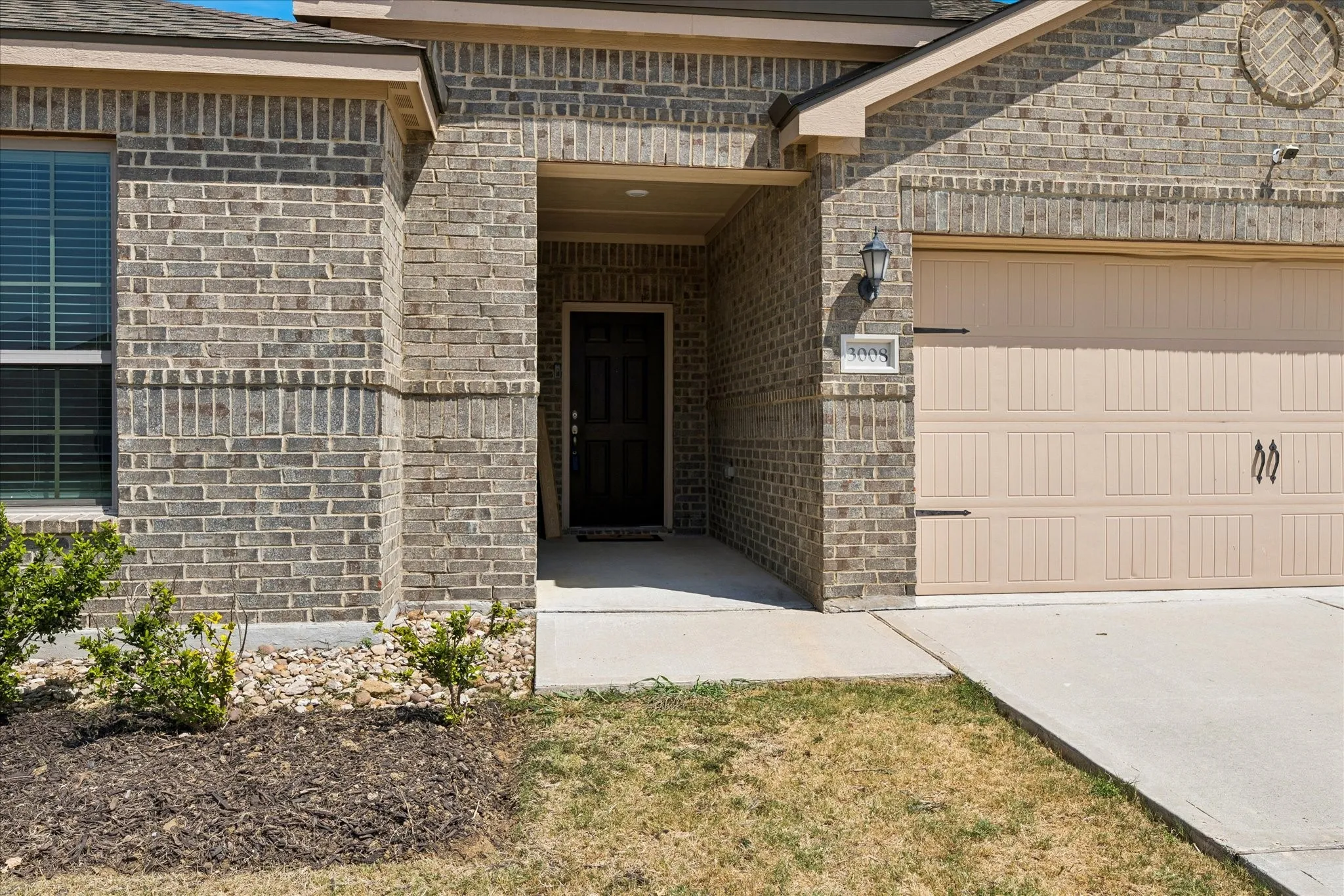 Brick exterior, covered entry, attached garage, concrete driveway, and established landscaping
