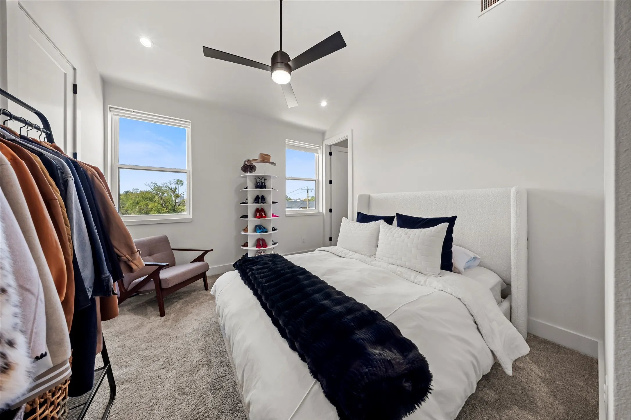 Bright primary bedroom showcasing white shaker-style wall paneling, a black ceiling fan with integrated lighting, and abundant natural light from dual windows