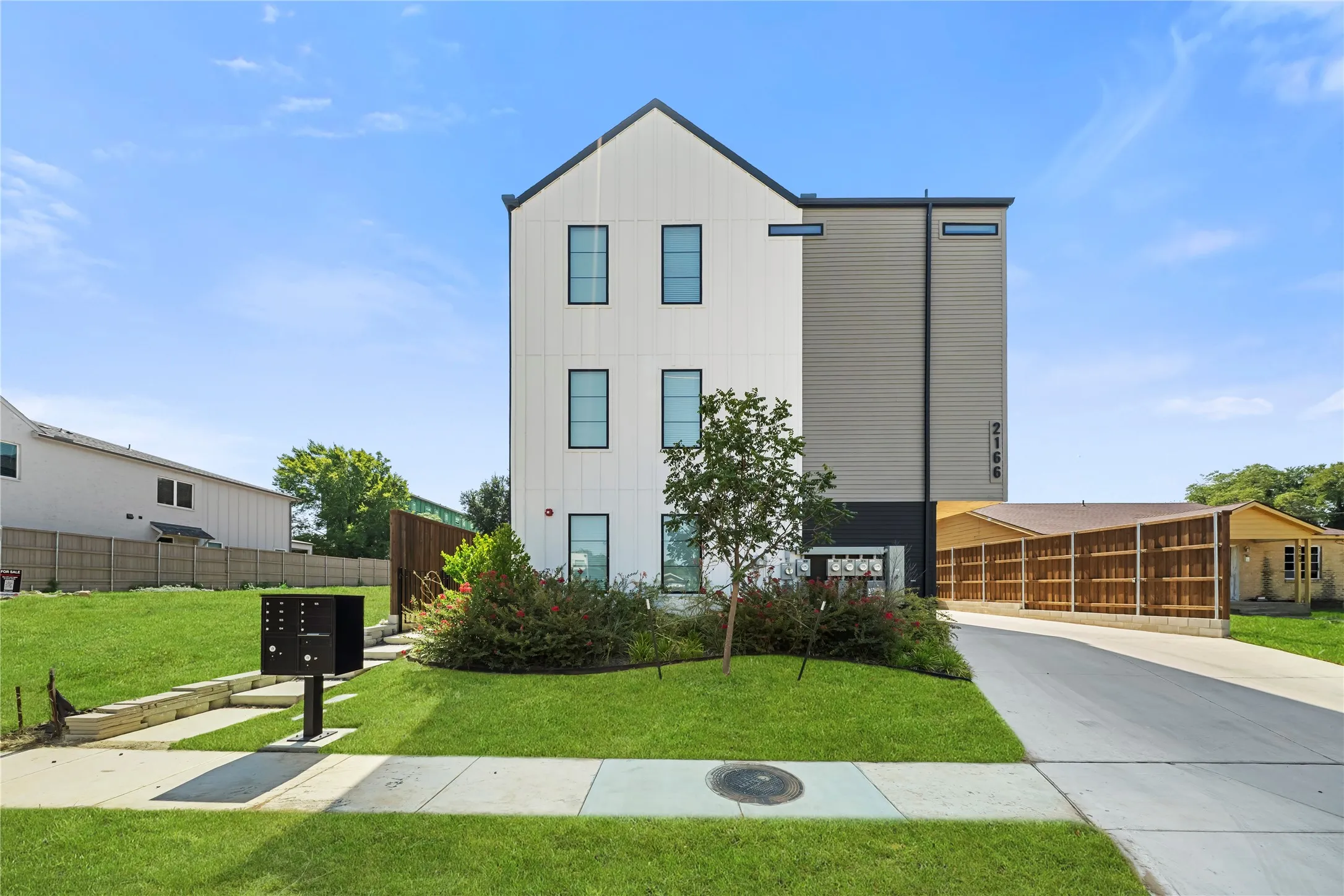 Contemporary exterior with white vertical siding and dark accents, featuring a paved driveway, manicured lawn, and landscaped shrubbery