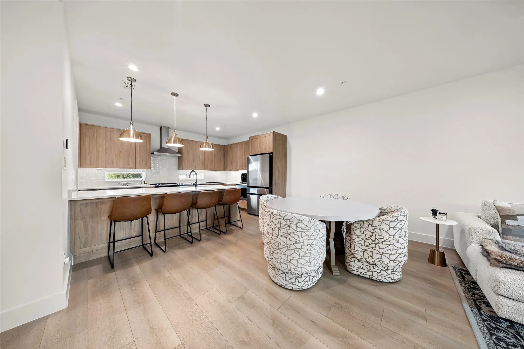 Open concept kitchen featuring wood-finish cabinetry, stainless steel appliances, a white tile backsplash, and a breakfast bar