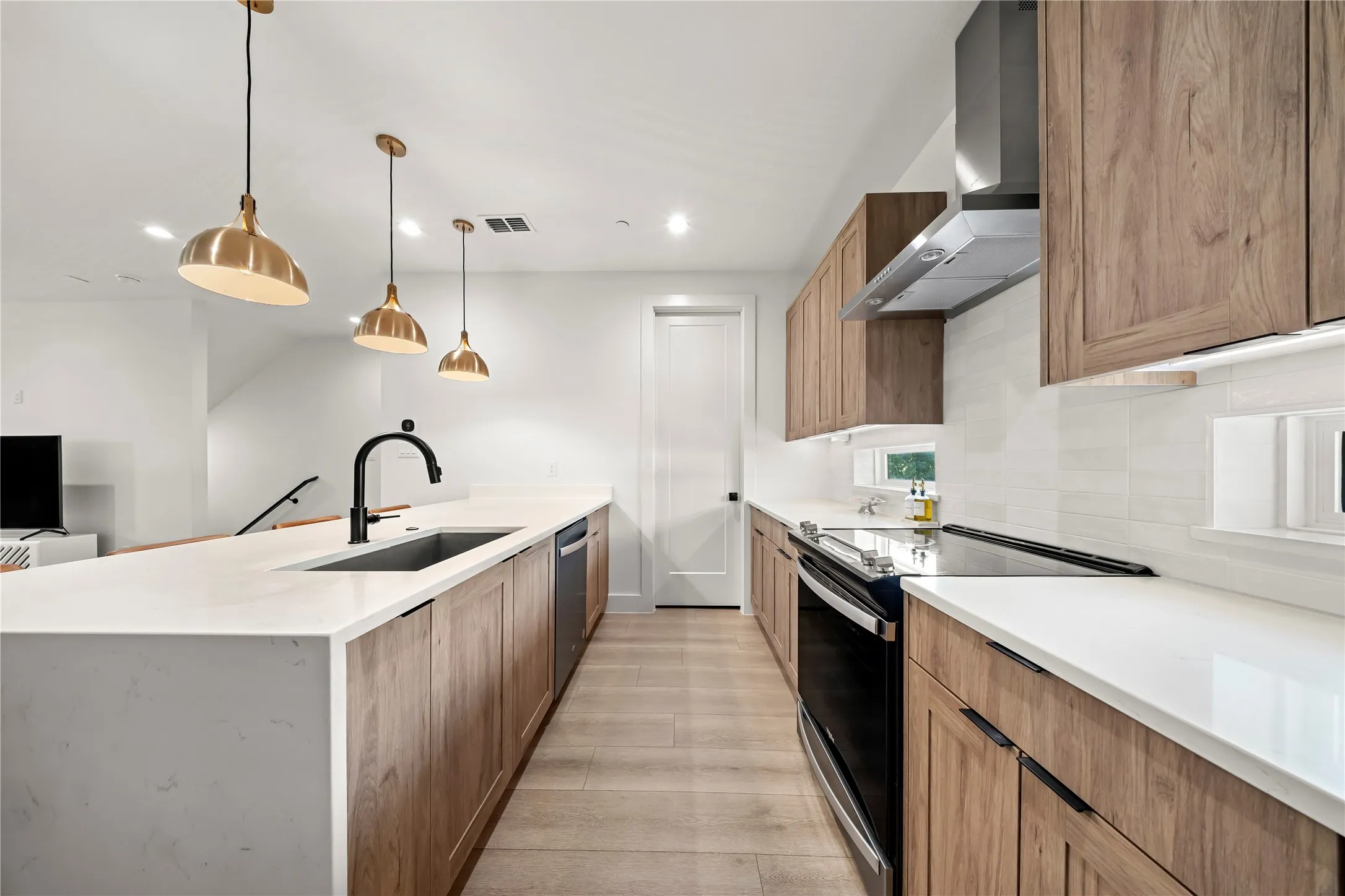 Modern kitchen featuring quartz countertops, wood-finish cabinetry, a stainless steel range hood, and a built-in dishwasher