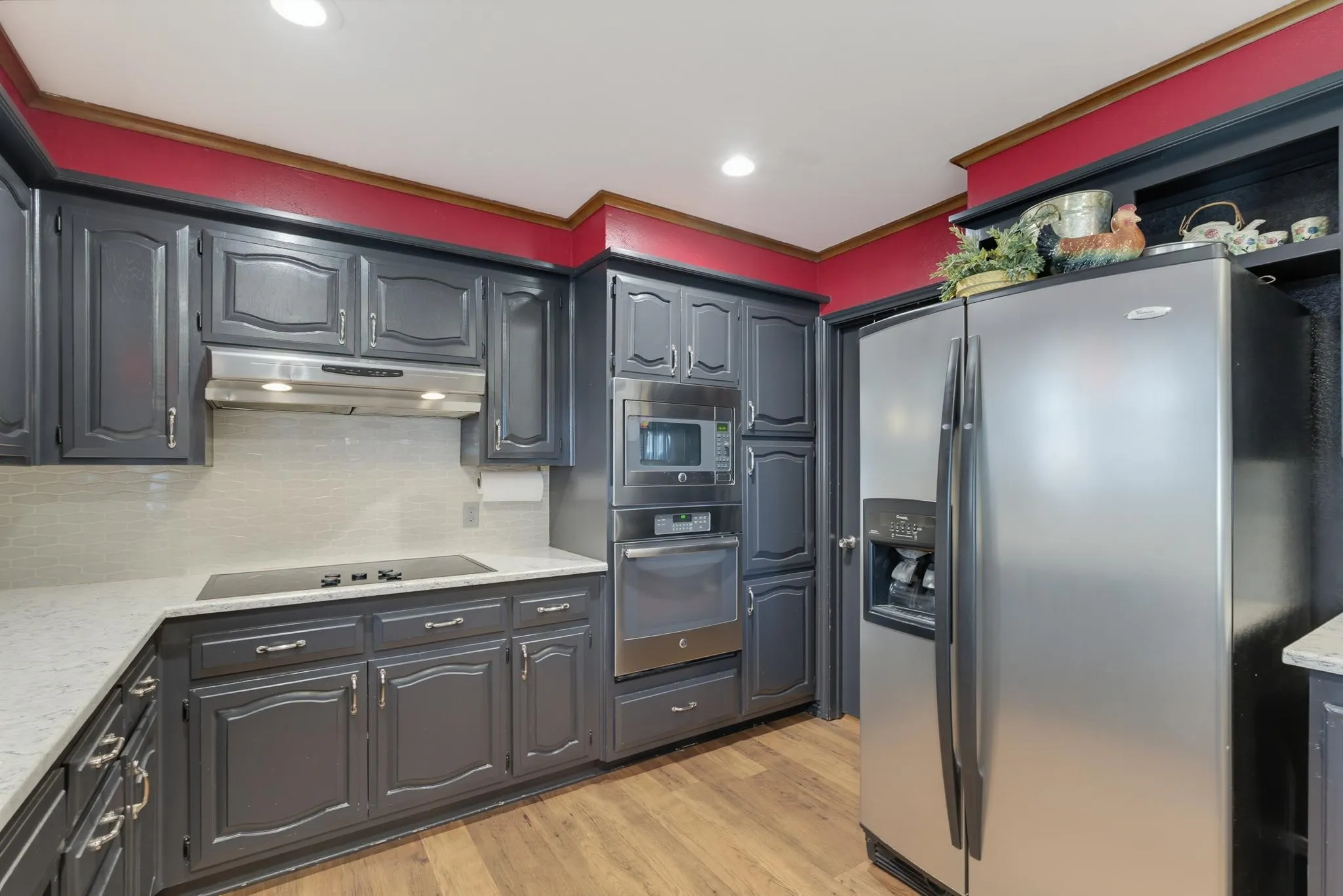 Kitchen featuring dark-painted cabinetry, light-toned countertops, tile backsplash, wood-finish flooring, and stainless steel appliances