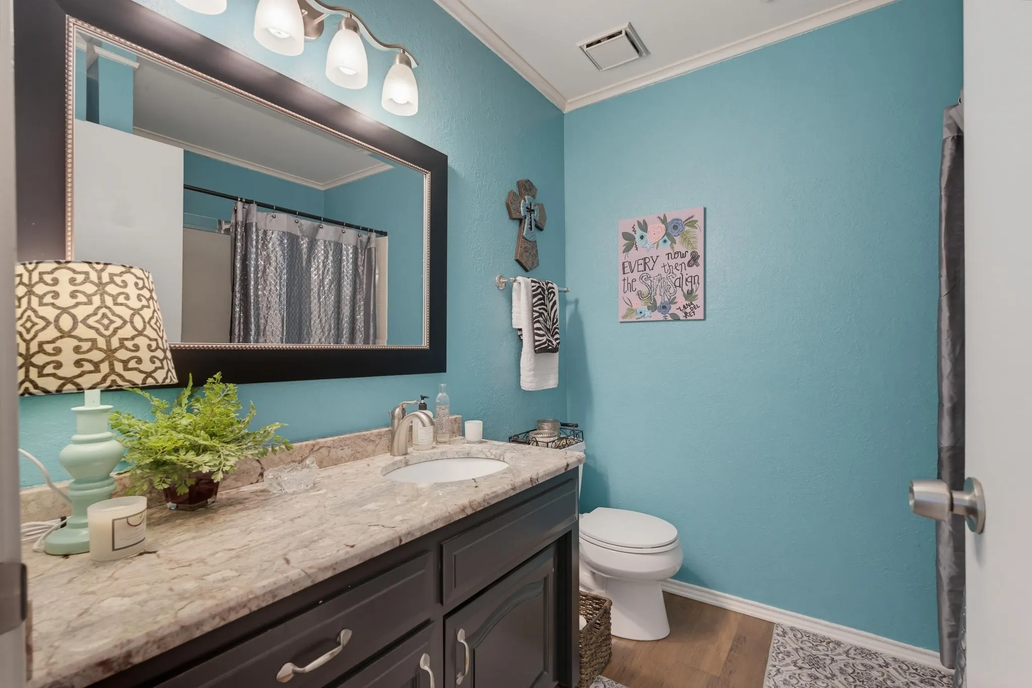 Spa-inspired bathroom featuring turquoise walls, a dark vanity with wood-finish countertop, large framed mirror with integrated lighting, and contemporary fixtures