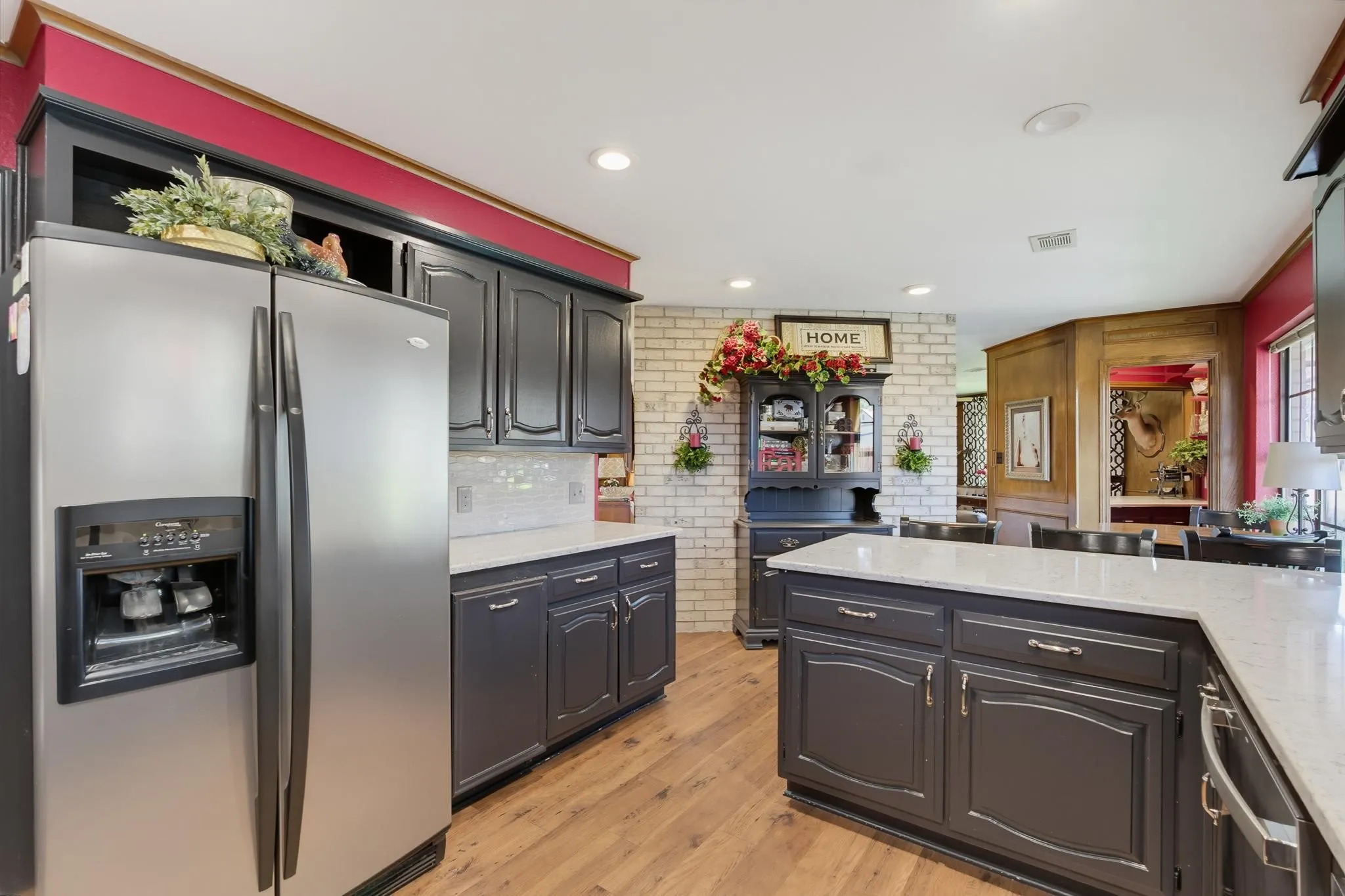 Stainless steel refrigerator, white countertops, dark cabinetry, wood-finish flooring, and a subway tile backsplash