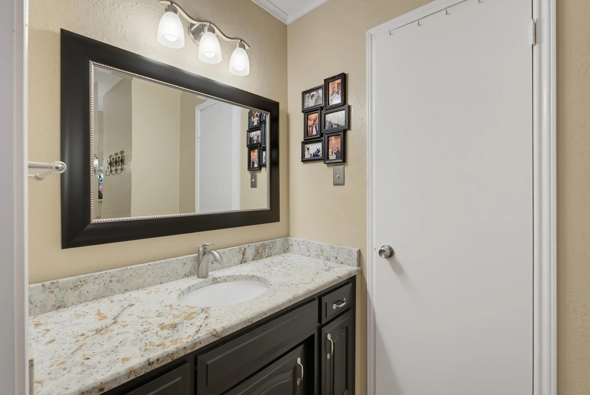 Built-in vanity with under-mount sink, speckled countertop, dark wood-finish cabinetry, and framed mirror with integrated lighting