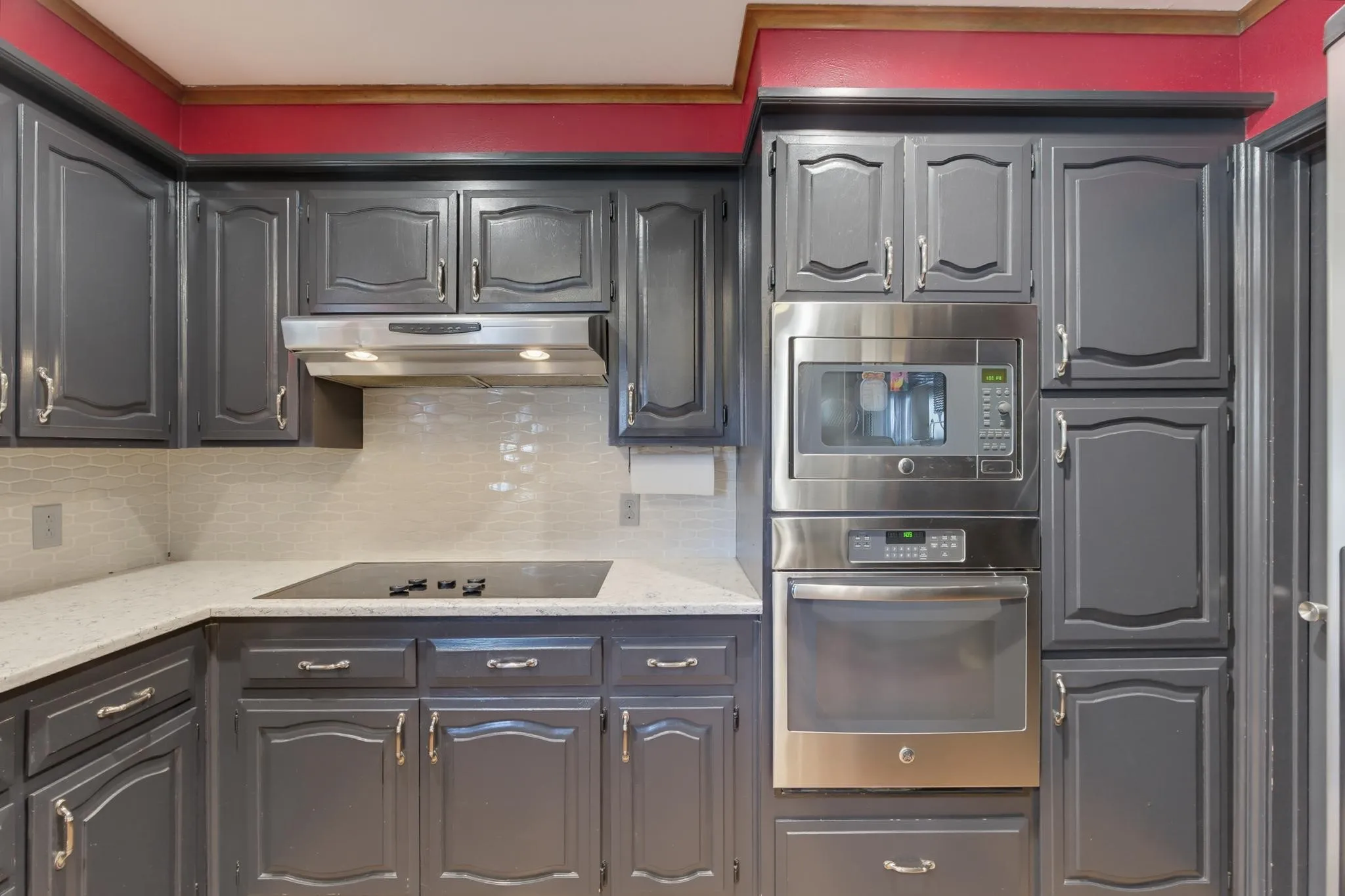Gray cabinetry with silver hardware, white countertop, white subway tile backsplash, stainless steel microwave, and built-in oven