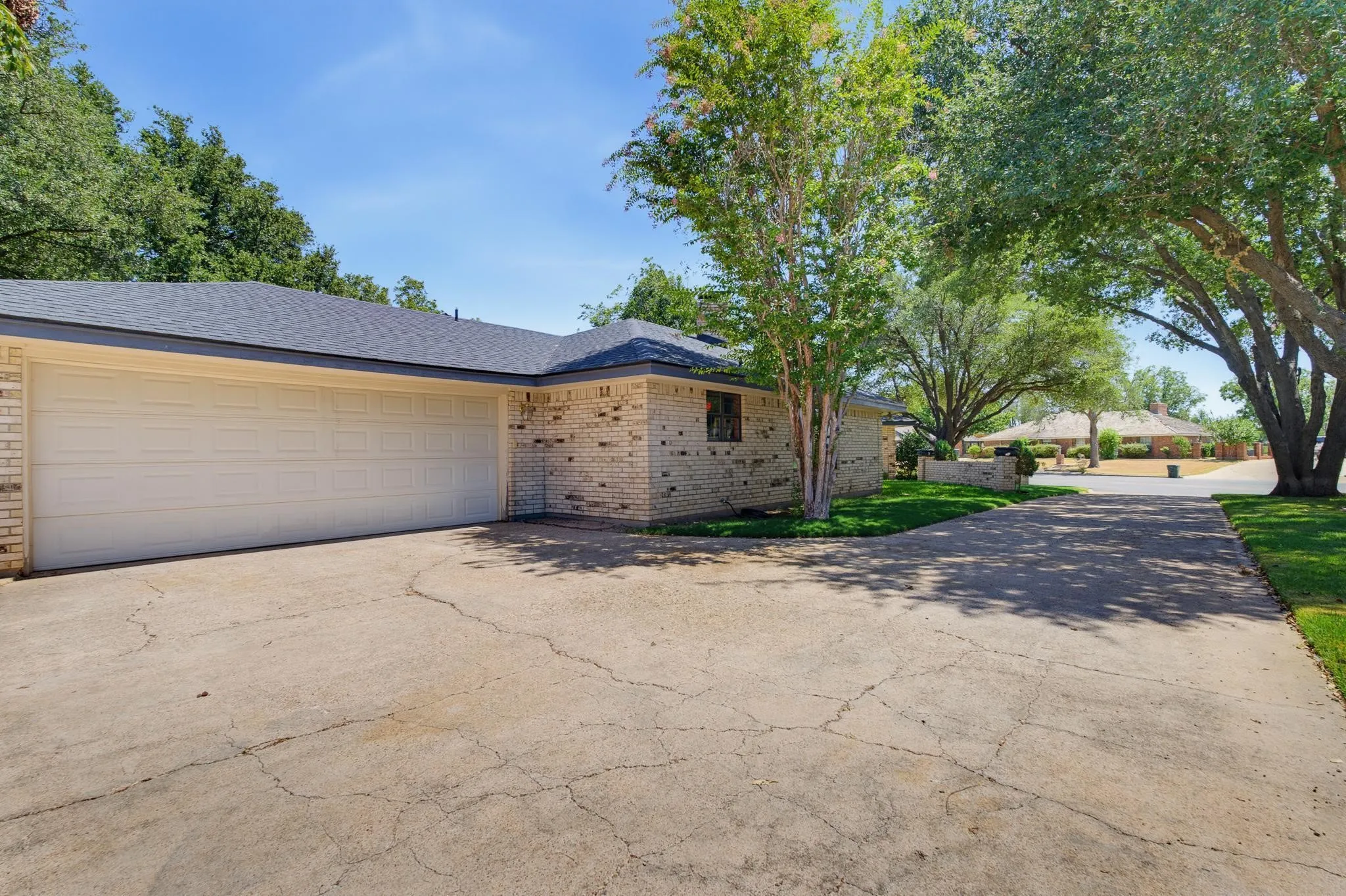 Brick exterior construction with a multi-car garage, mature shade trees, and a concrete driveway