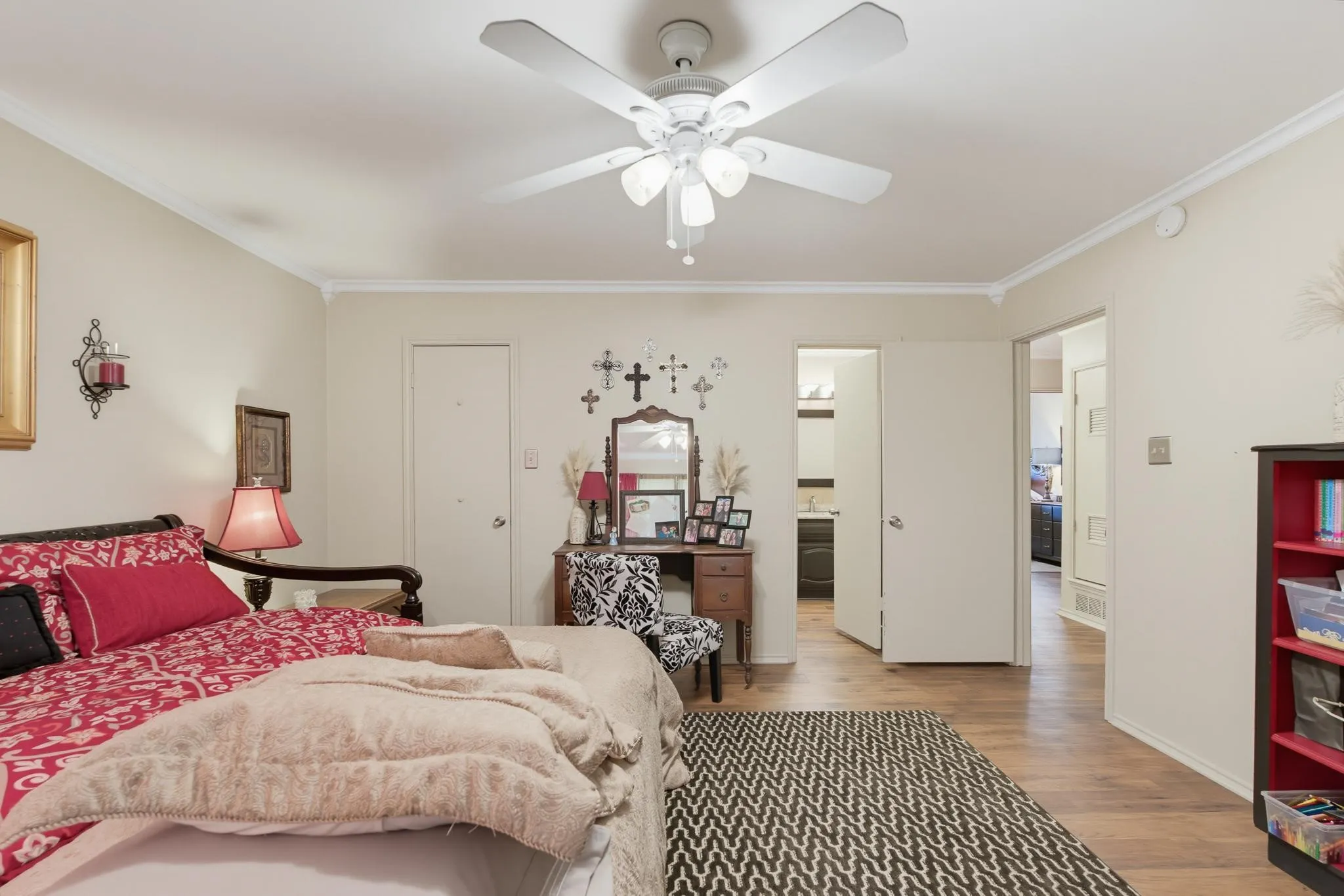 Spacious primary bedroom featuring hardwood flooring, ceiling fan with integrated lighting, multiple closet entries, and an ensuite bathroom