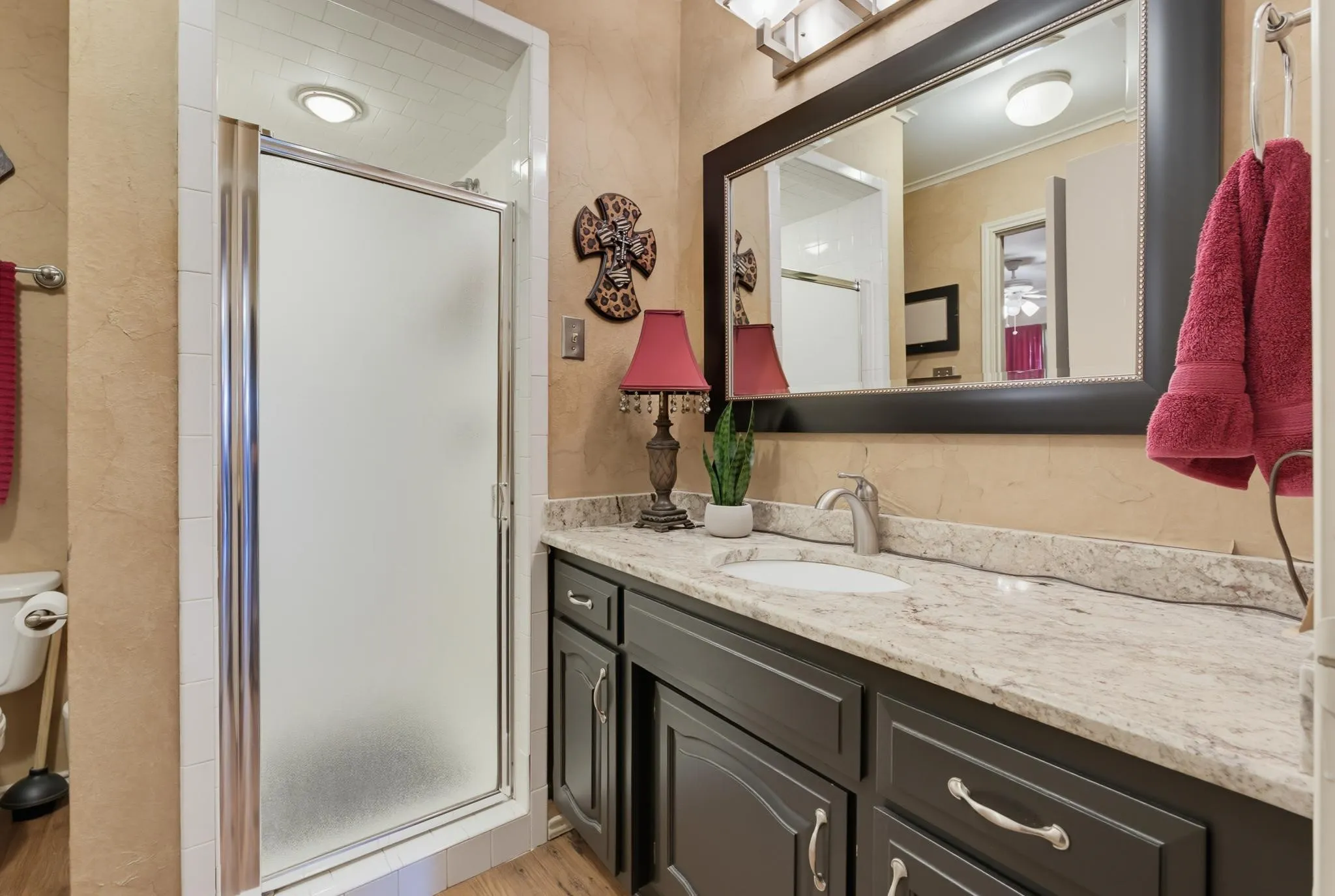 Spa-inspired master bathroom featuring a dark wood vanity with marble-topped countertop, large framed mirror with integrated lighting, and a walk-in shower with frosted glass enclosure and chrome fixtures
