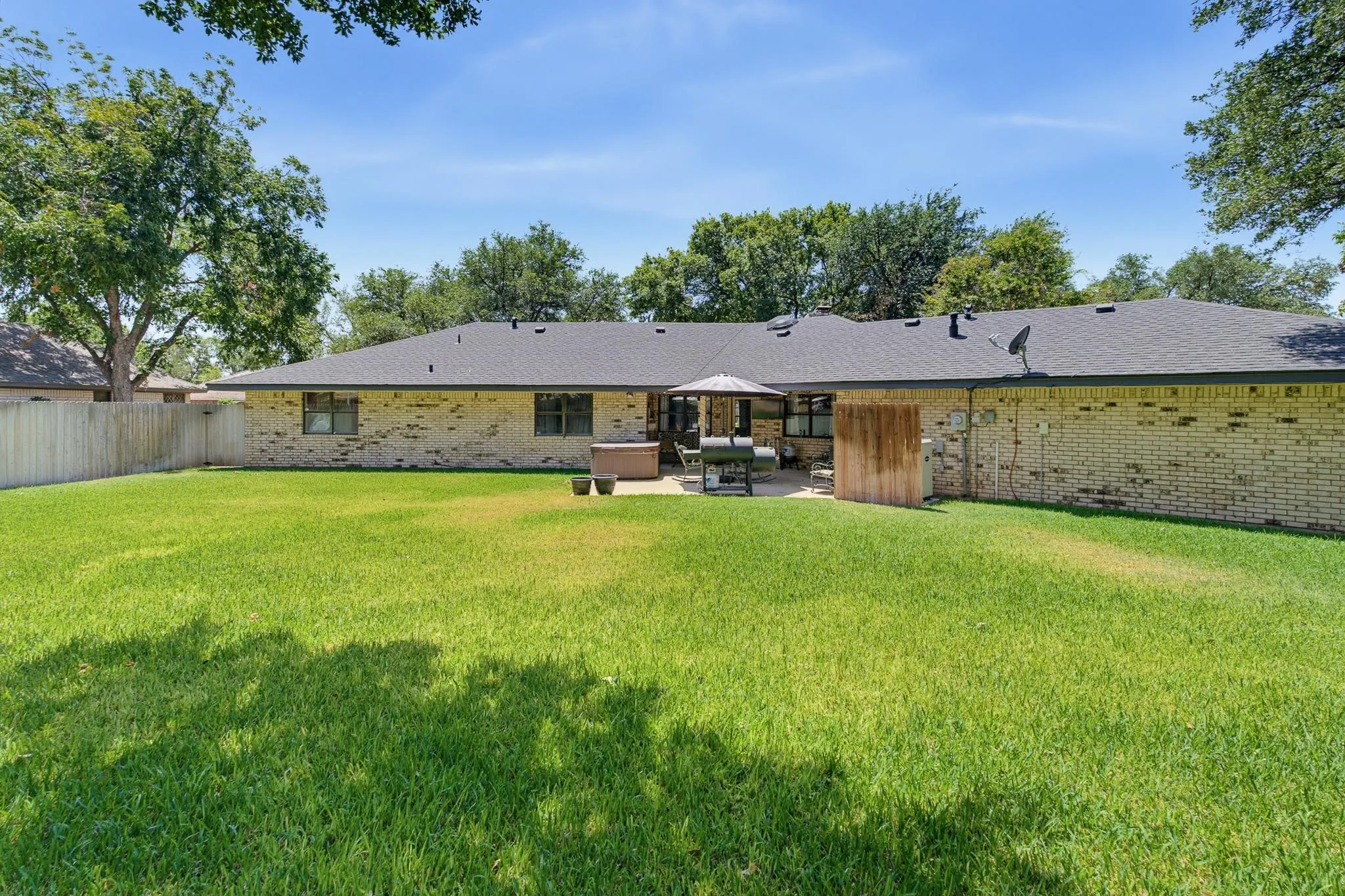 Expansive backyard with a manicured lawn, brick exterior, and a paved patio area