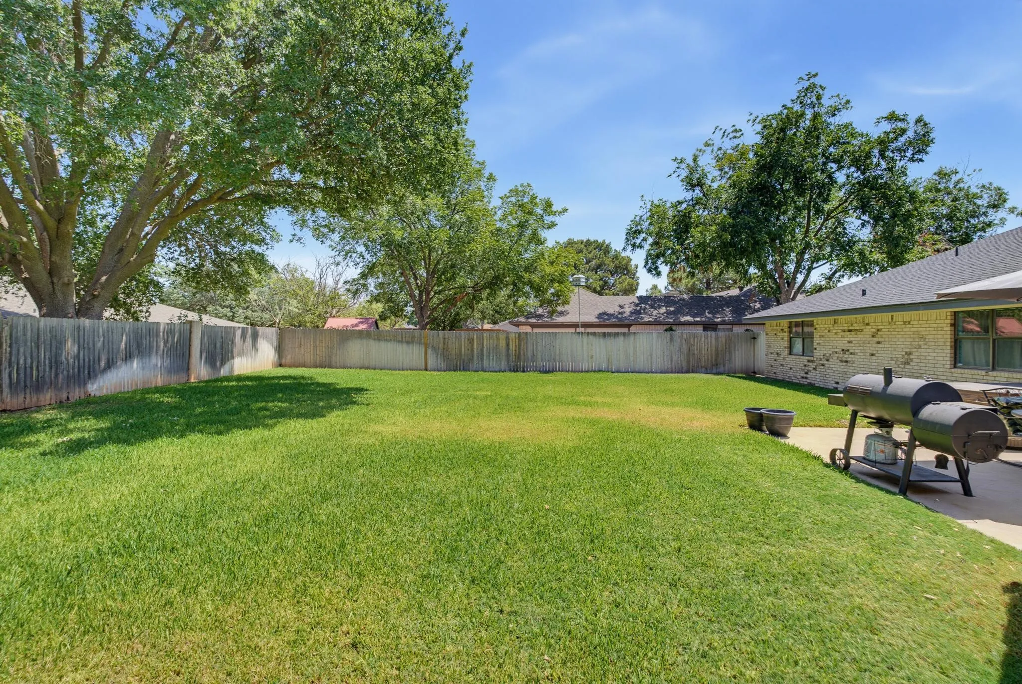 Expansive backyard featuring a manicured lawn, full perimeter wood fencing, and mature trees