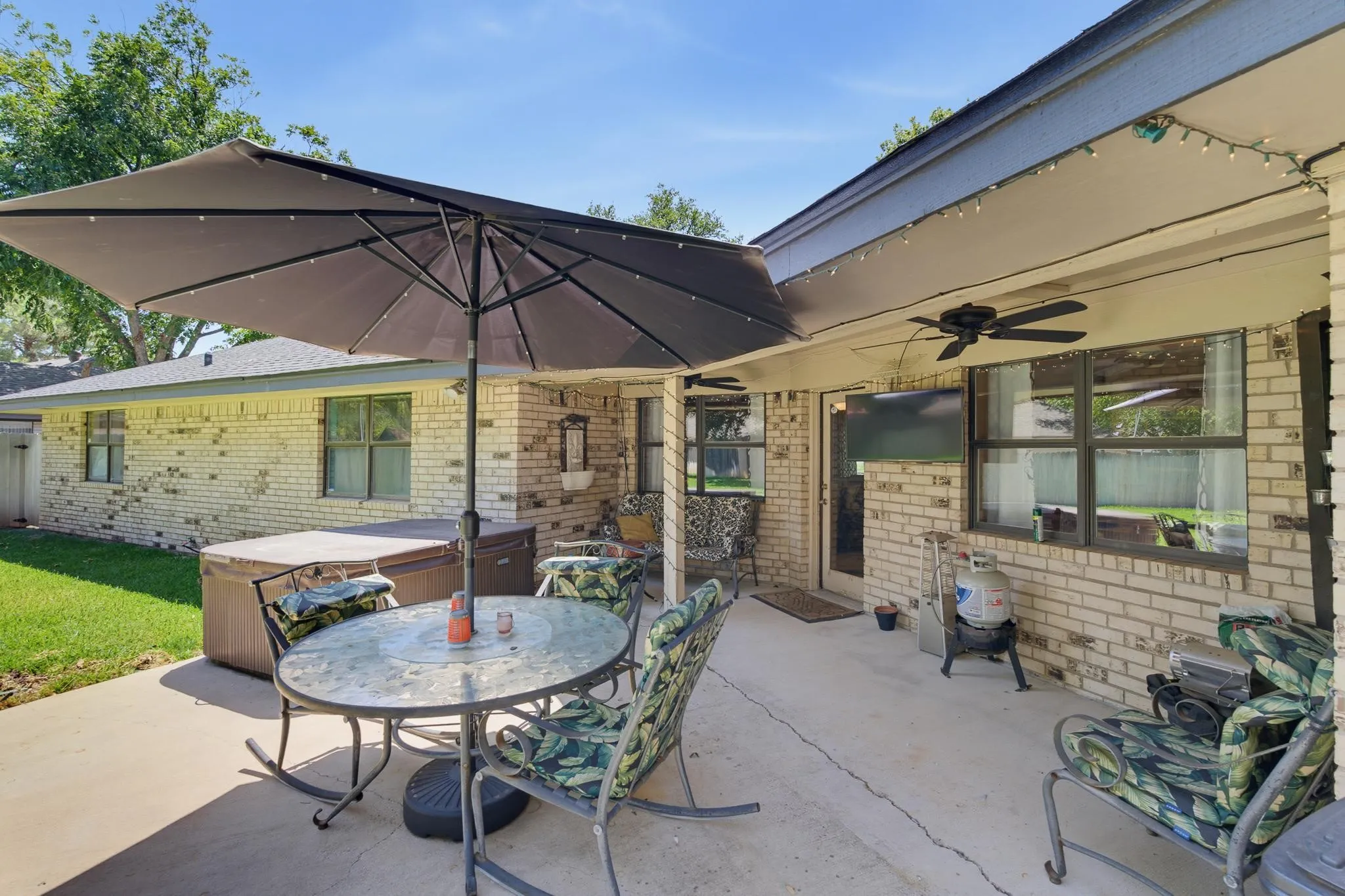 Expansive concrete patio featuring a hot tub, brick exterior, and a covered section with a ceiling fan