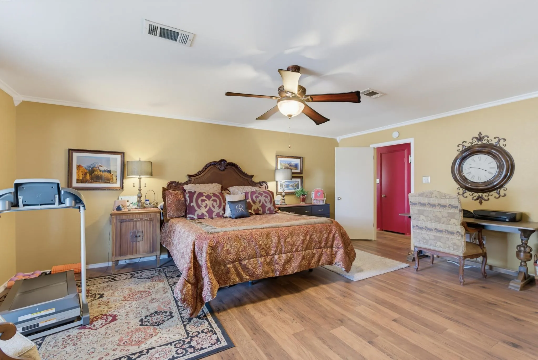 Spacious primary bedroom with warm yellow walls, wood-finish flooring, and a ceiling fan with integrated lighting