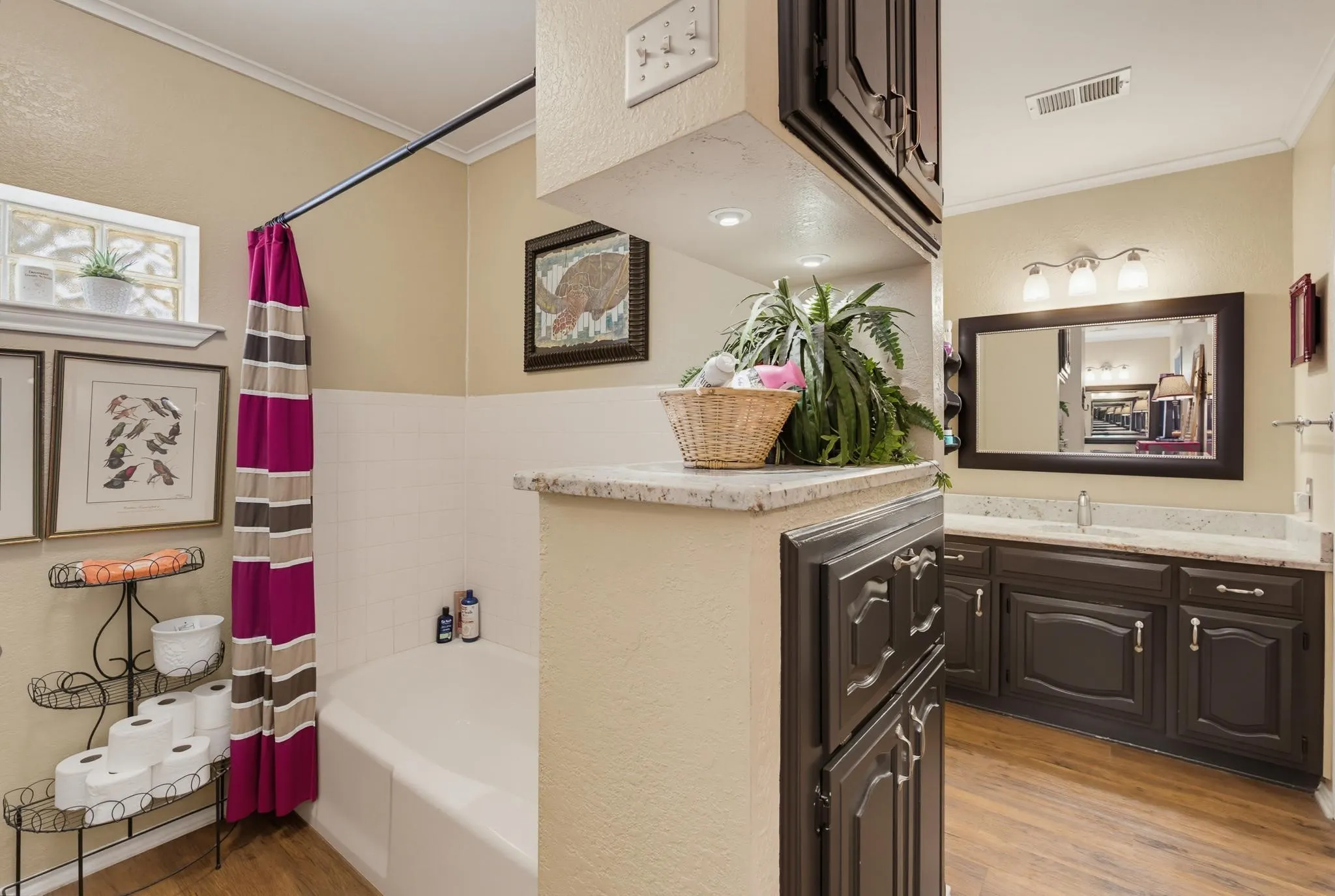 Built-in bathtub, light-toned wall paint, wood-finish flooring, built-in vanity with light-toned countertop, and dark wood-finish cabinetry