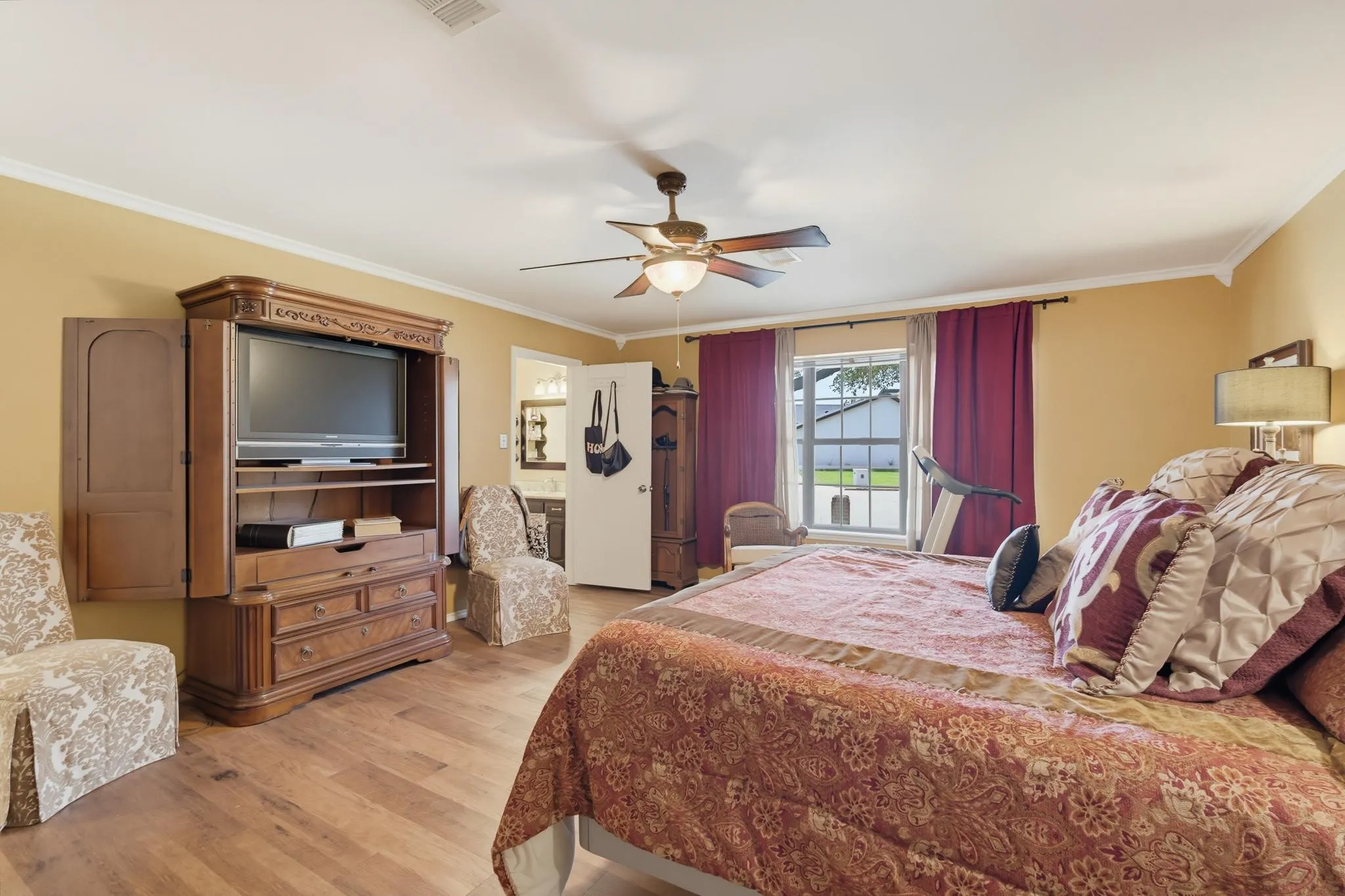 Wood-finish flooring, ceiling fan with integrated lighting, crown molding, and a window providing natural light