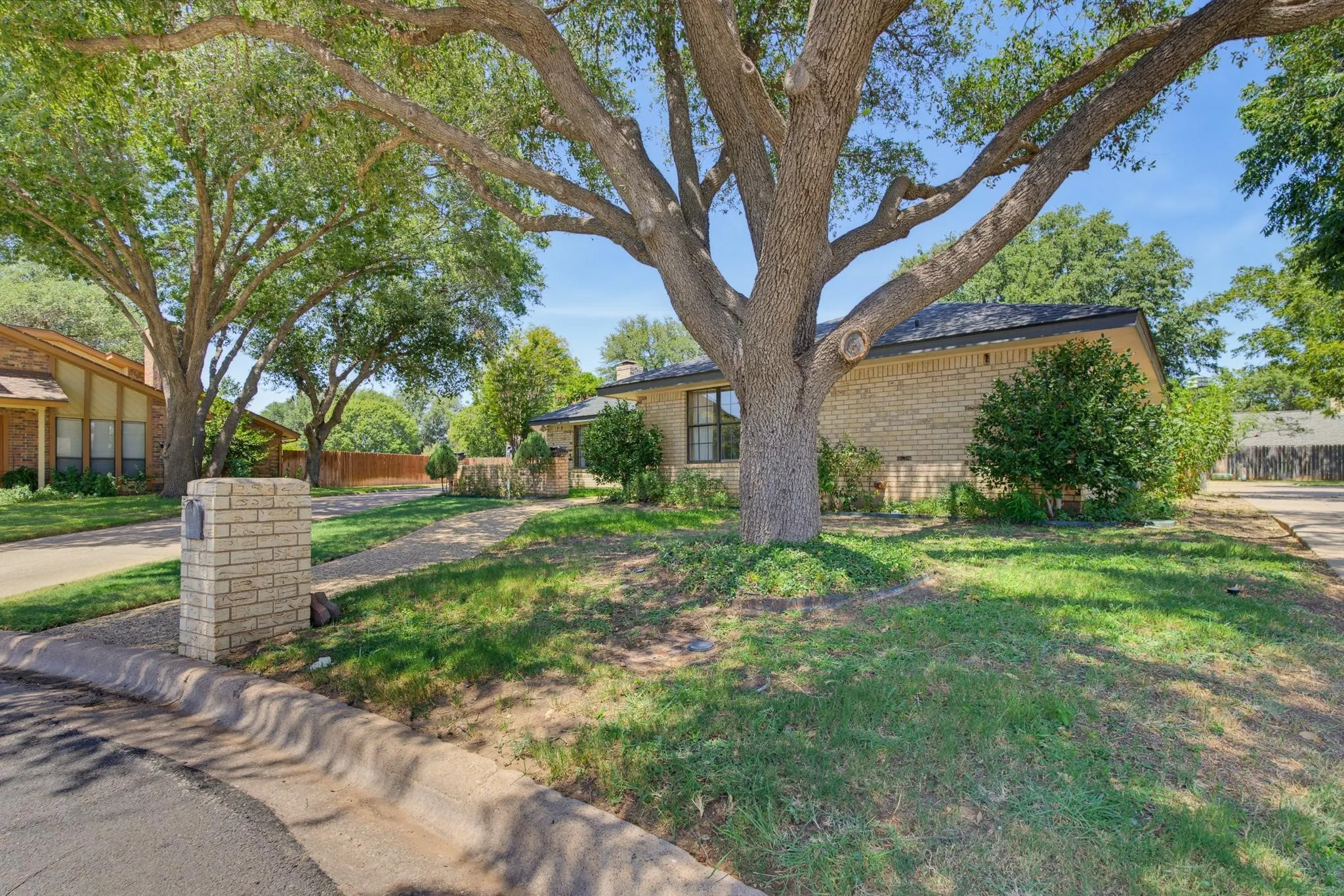 Brick exterior with a dark shingle roof, mature trees, a driveway, and a brick mailbox pillar