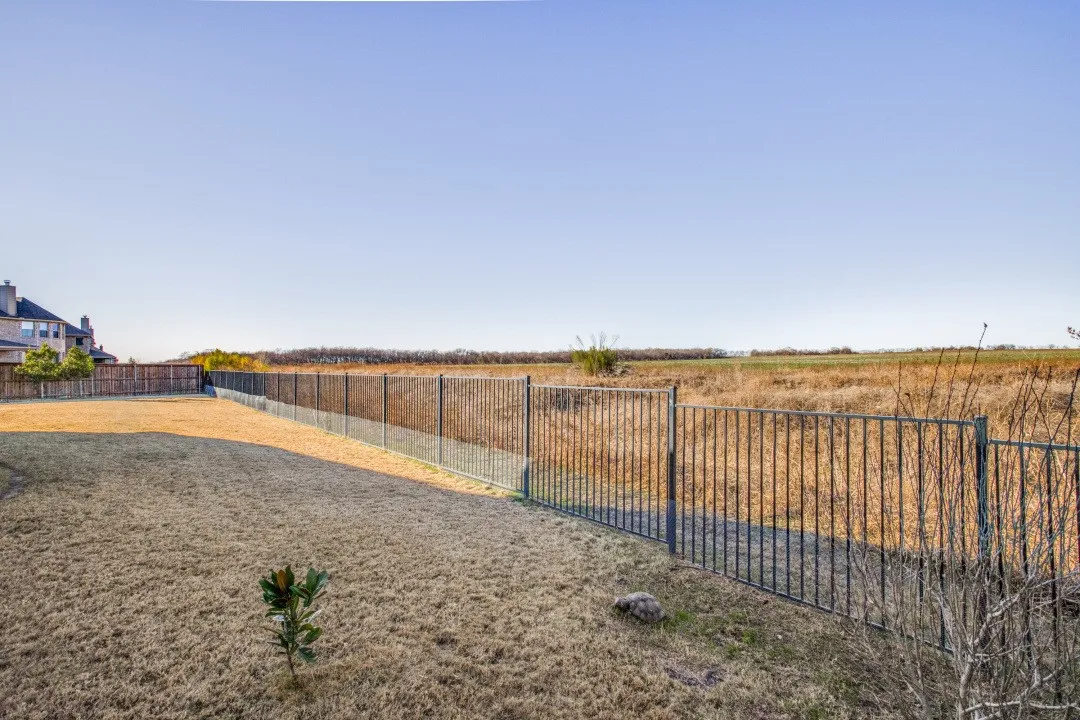 Expansive backyard featuring a wrought iron fence, wood privacy fencing, and a manicured lawn