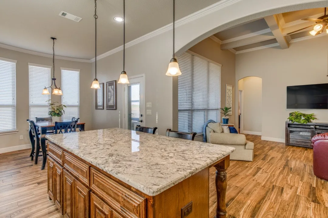 Spacious kitchen island with light-toned countertop, wood-finish flooring, recessed lighting, and decorative pendant light fixtures