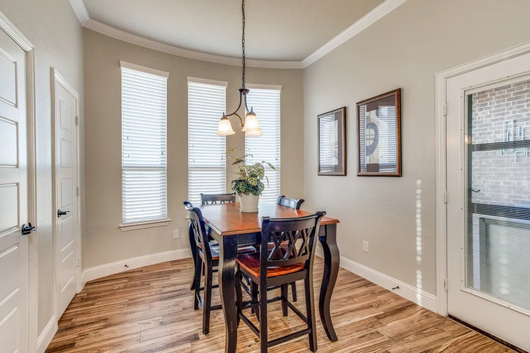 Wood-finish flooring, crown molding, three vertical windows, pendant light fixture, and a glass-paneled door