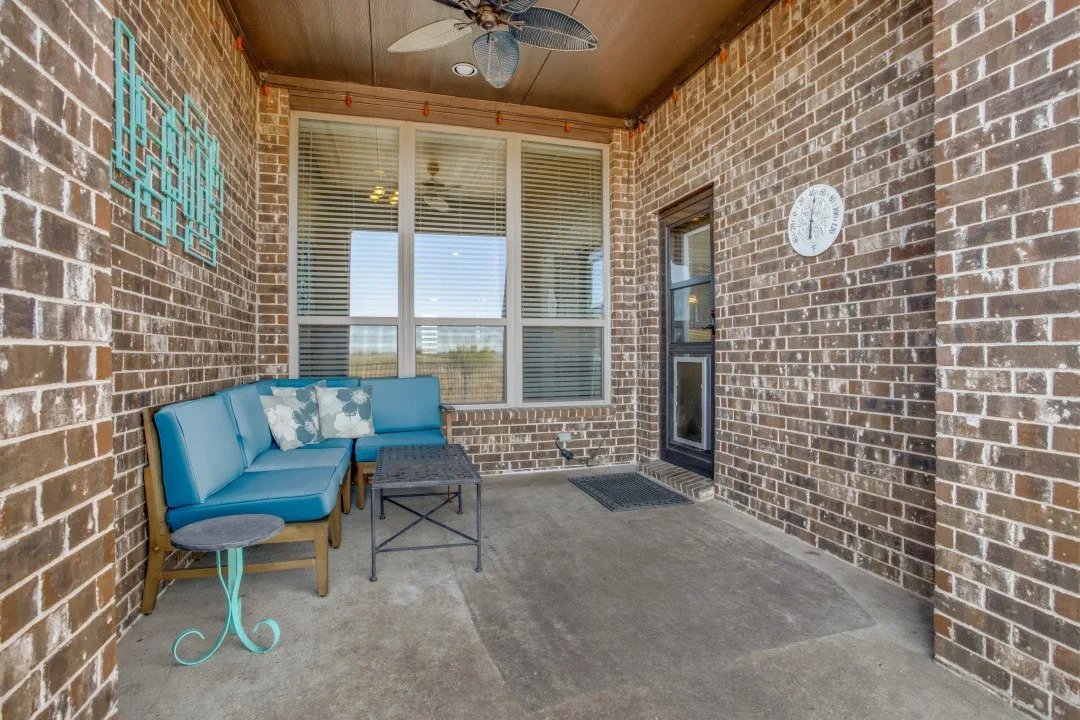 Covered porch with exposed brick walls, ceiling fan, large multi-pane windows with blinds, and concrete flooring
