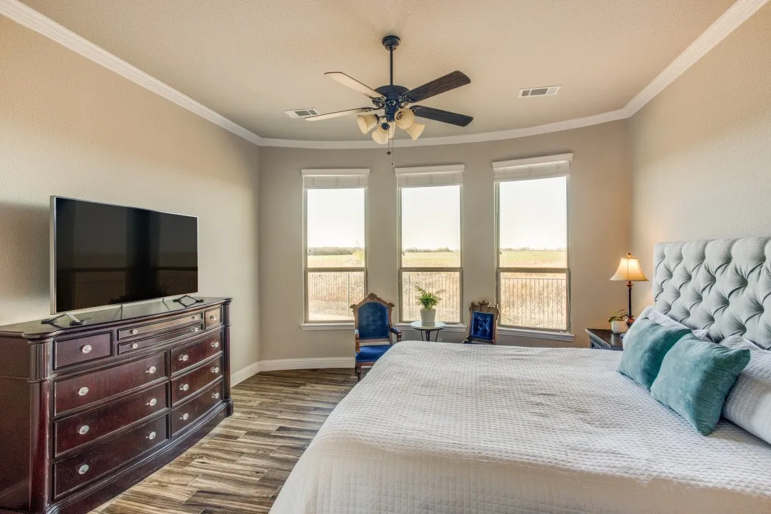 Recessed ceiling, wood-finish flooring, ceiling fan with light fixture, three windows, and crown molding