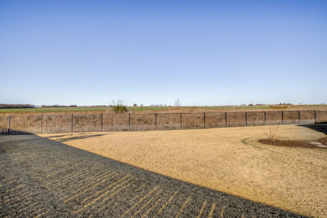 Expansive backyard with a metal fence, open field beyond, and a small landscaped bed