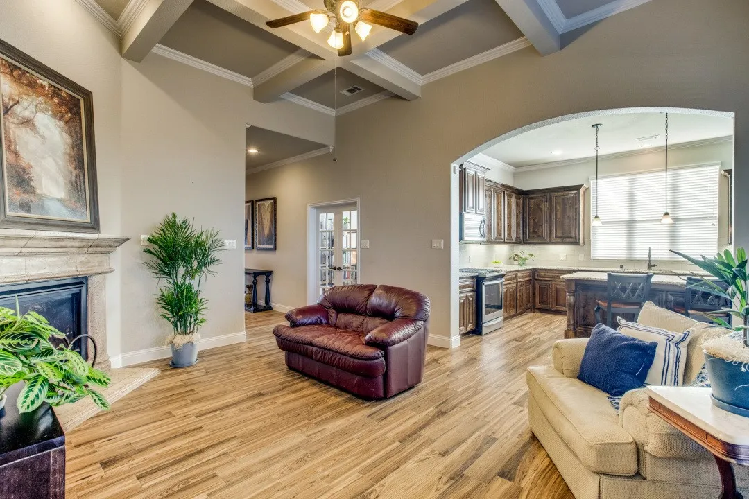 Vaulted ceiling with exposed beams, wood-finish flooring, stone fireplace, arched doorway, and built-in kitchen cabinetry