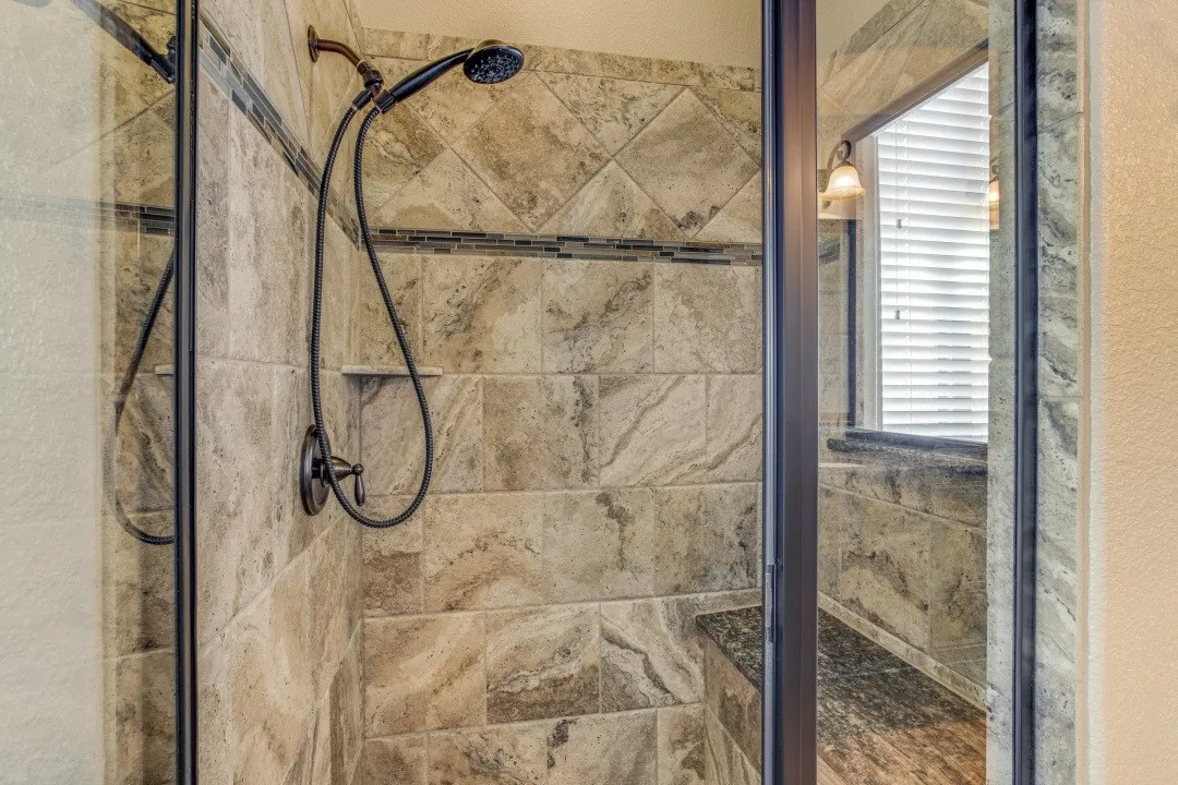 Walk-in shower featuring tiled walls with decorative accents, an integrated shower bench, and a handheld showerhead