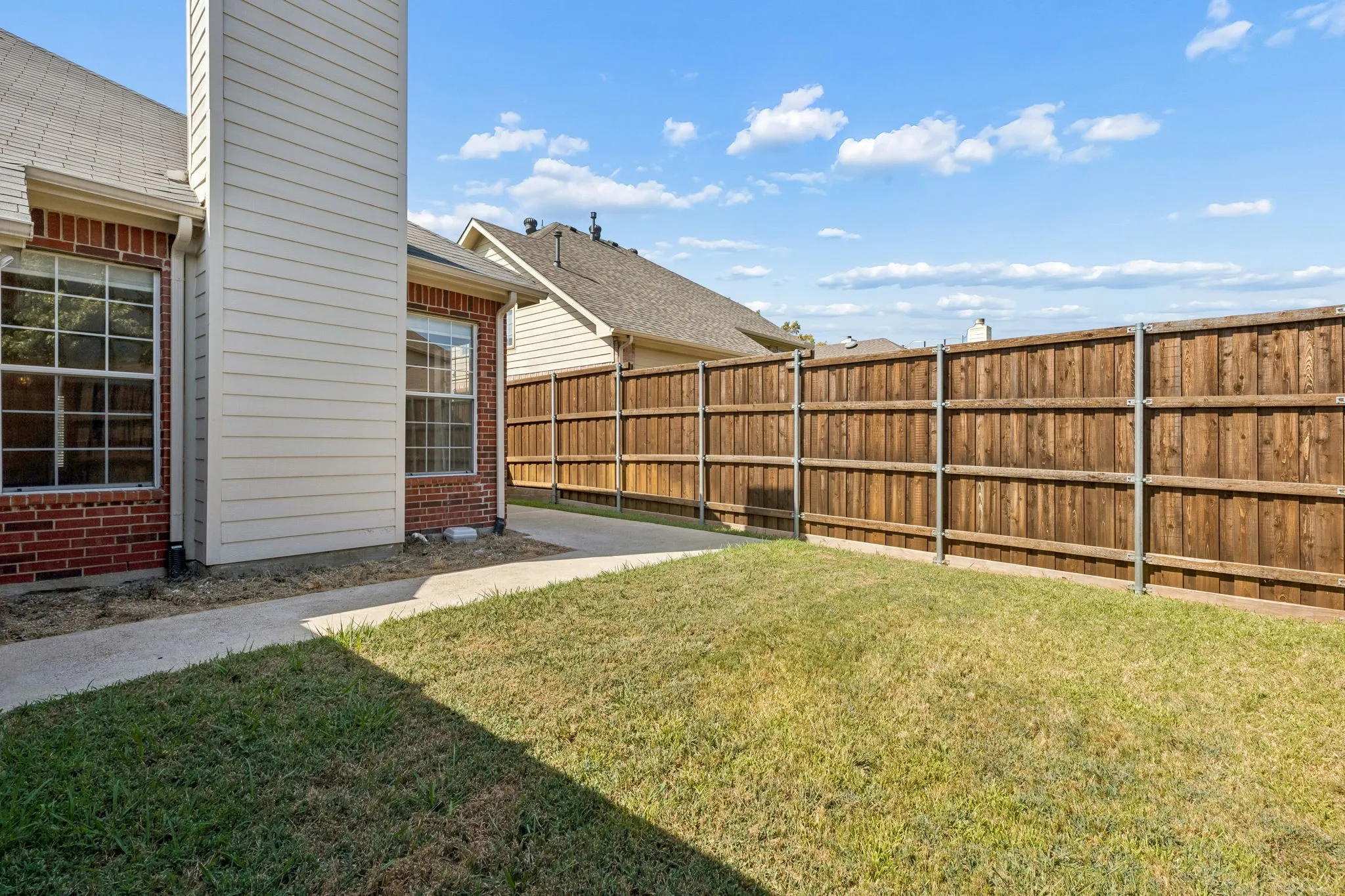 Grass lawn with a wood plank privacy fence and concrete walkway