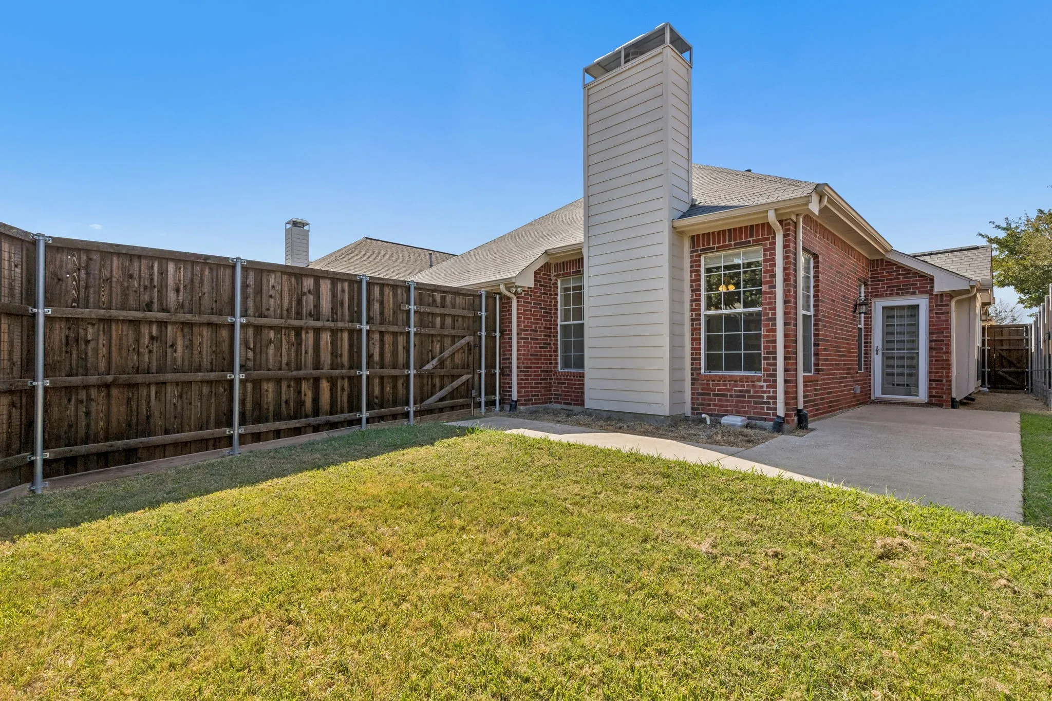 Brick exterior with a prominent chimney, concrete patio, and fenced yard