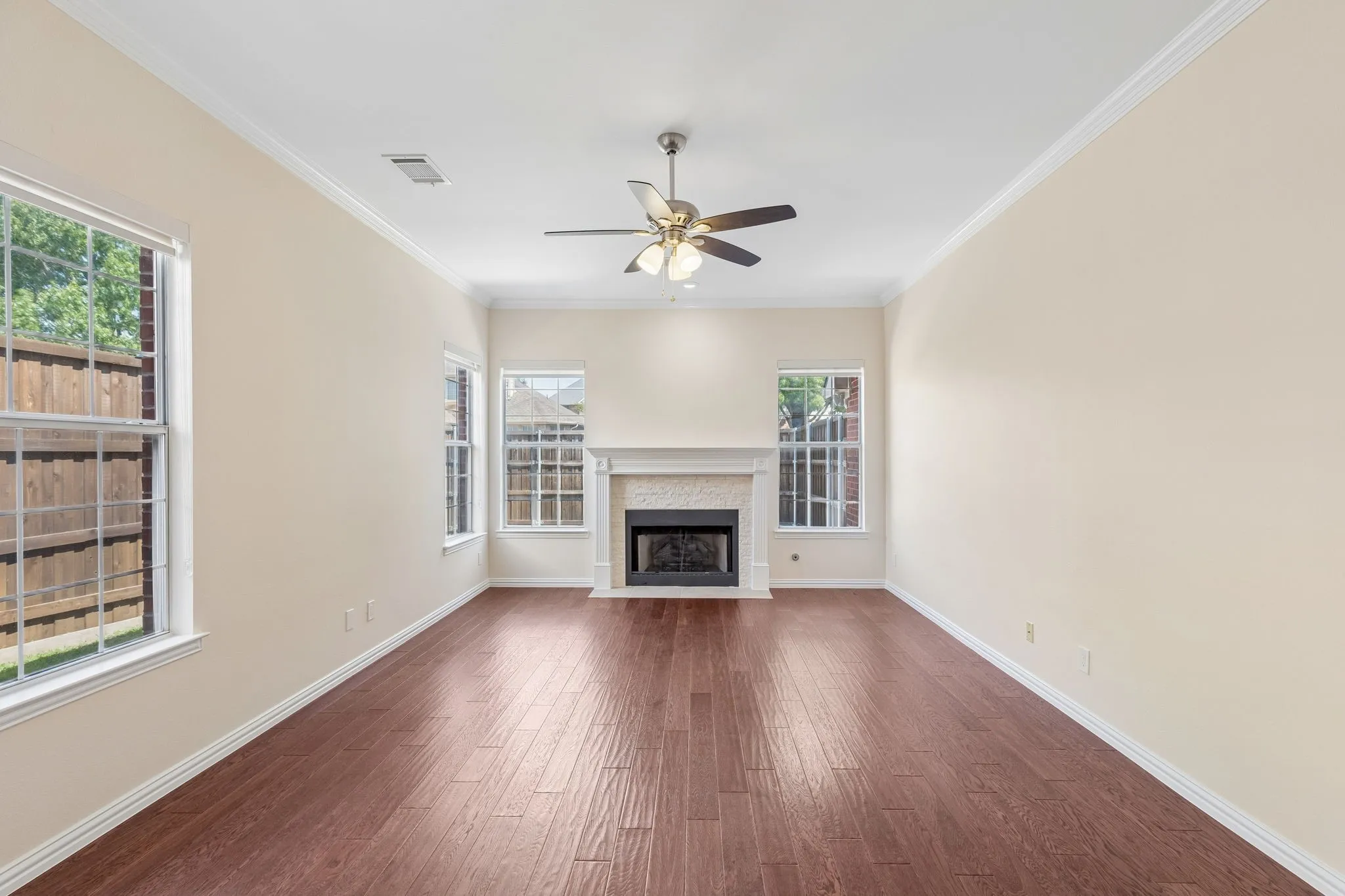 Spacious room featuring wood-finish flooring, a ceiling fan, crown molding, and multiple windows