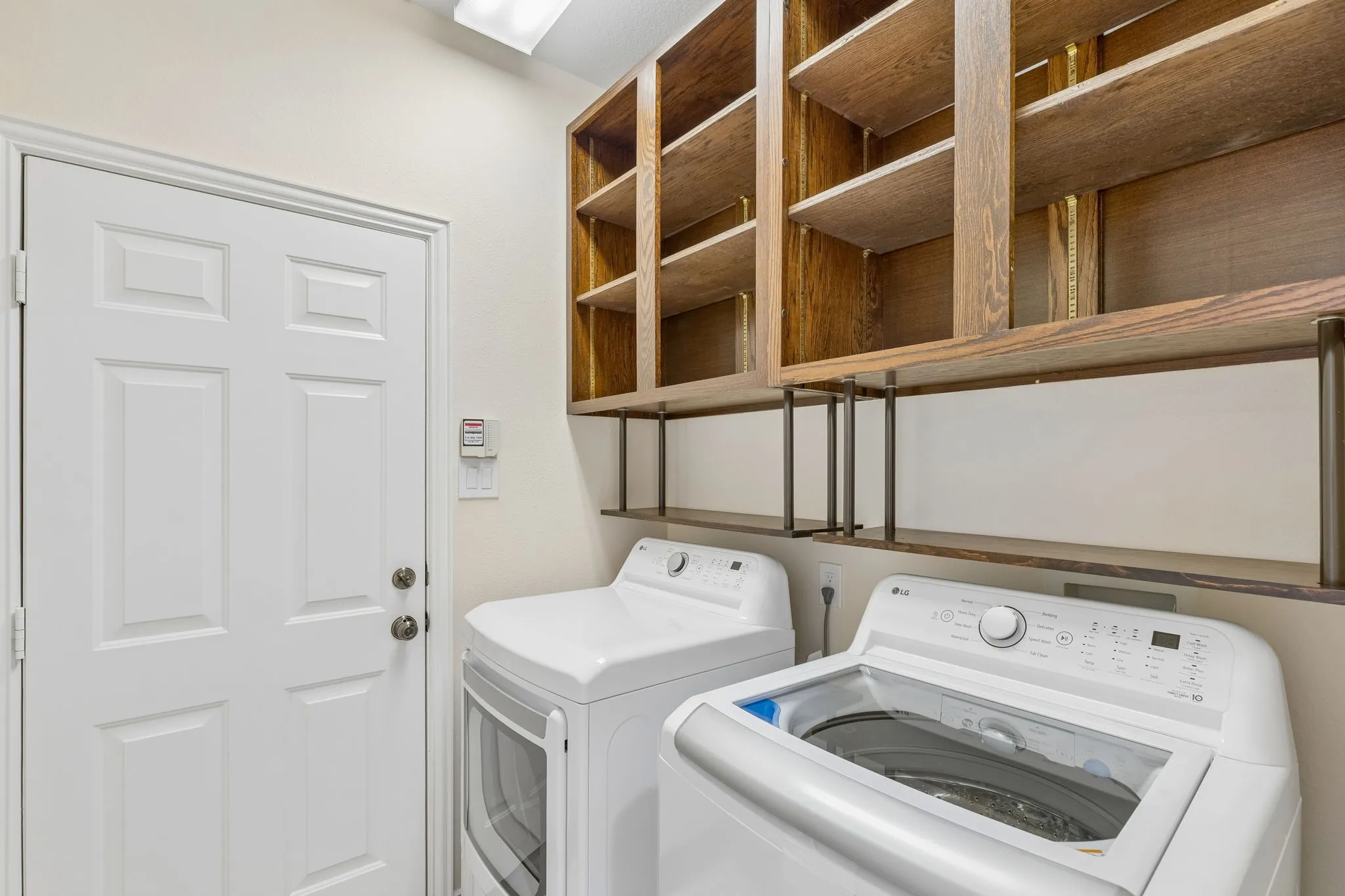 Laundry area featuring built-in wood-finish shelving, an overhead light fixture, and a white panel door