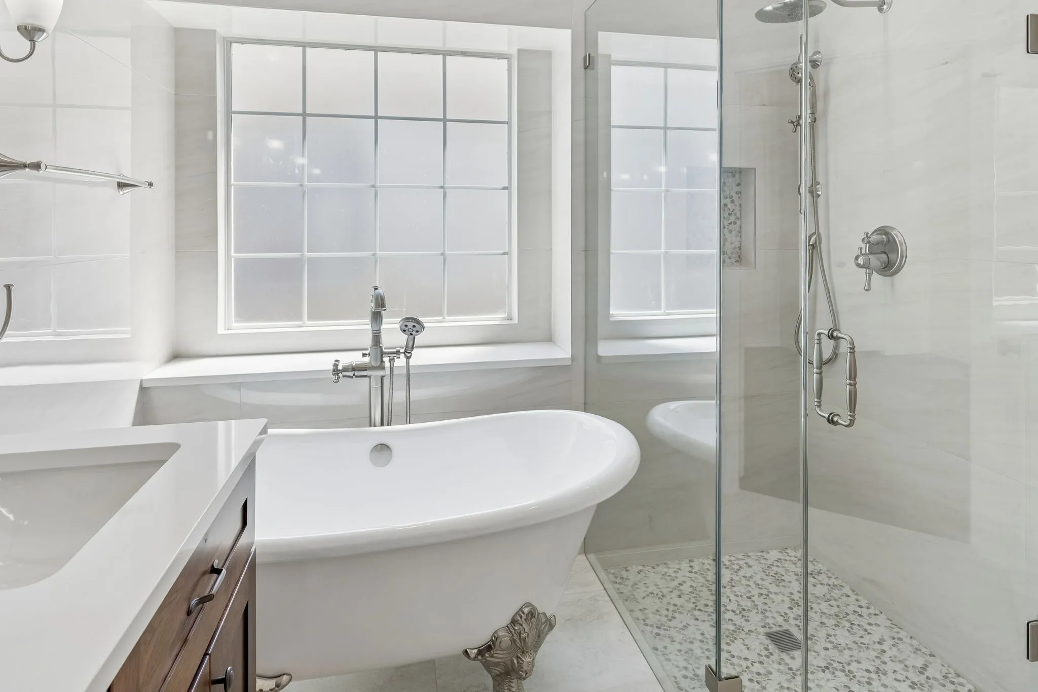Freestanding tub with claw feet, glass-enclosed shower, wood-finish vanity with countertop, and an opaque window
