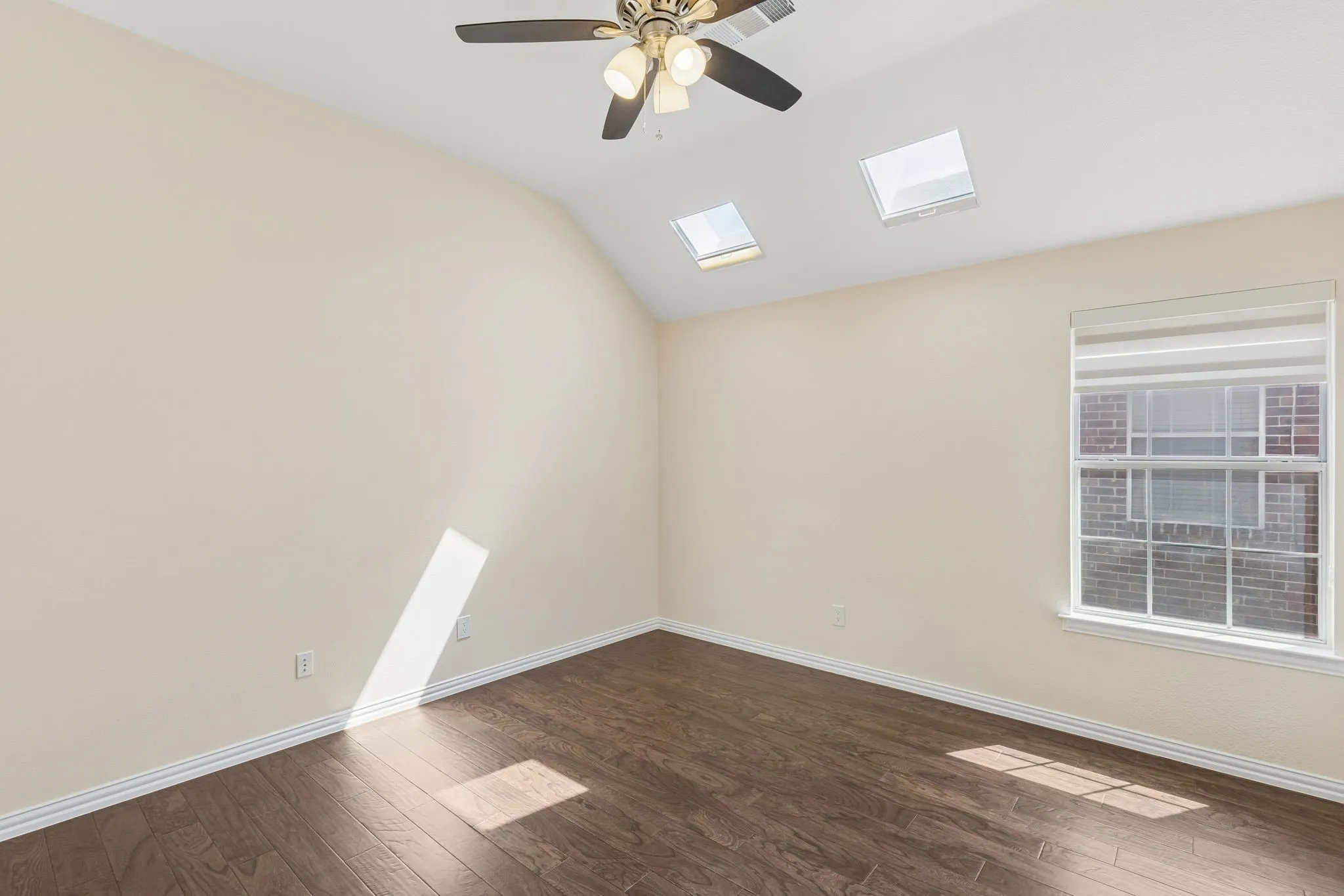 Vaulted ceiling with dual skylights, wood-finish flooring, and a ceiling fan with integrated lighting