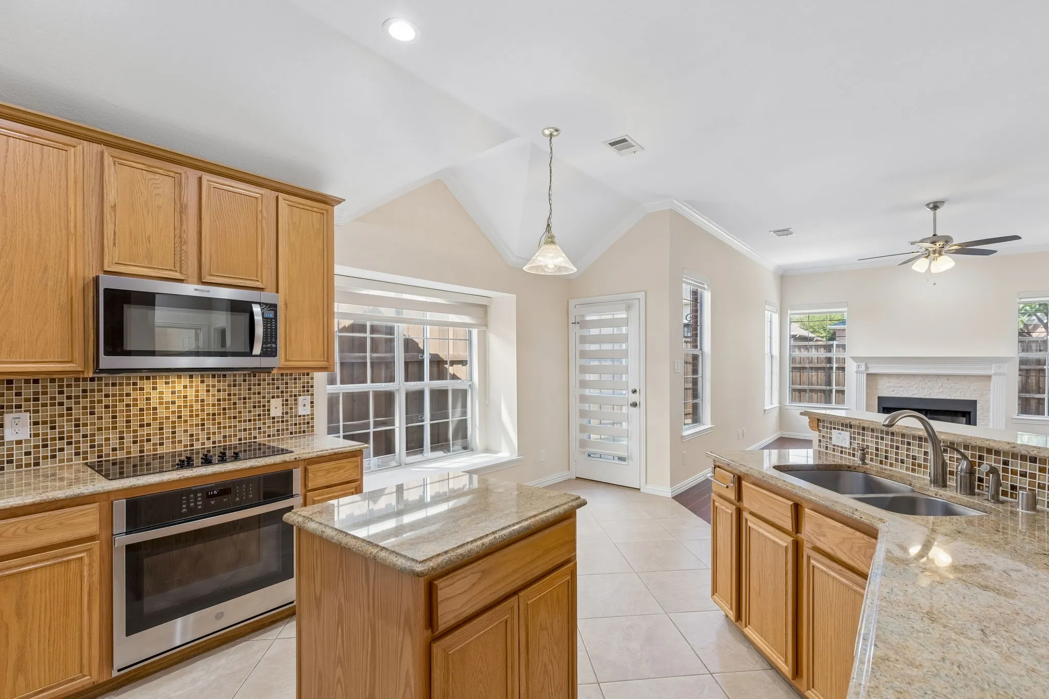 Kitchen featuring light wood cabinetry, stainless steel appliances, granite countertops, and a tile backsplash